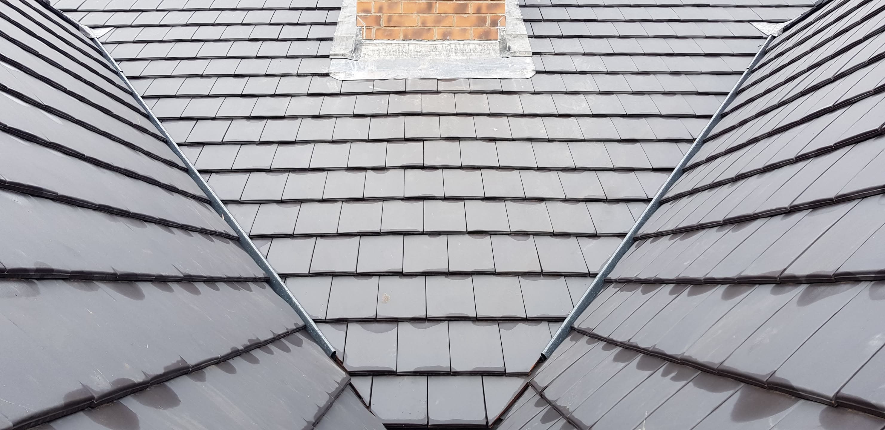 Grey slate pitched roof with valley and brick chimney stack