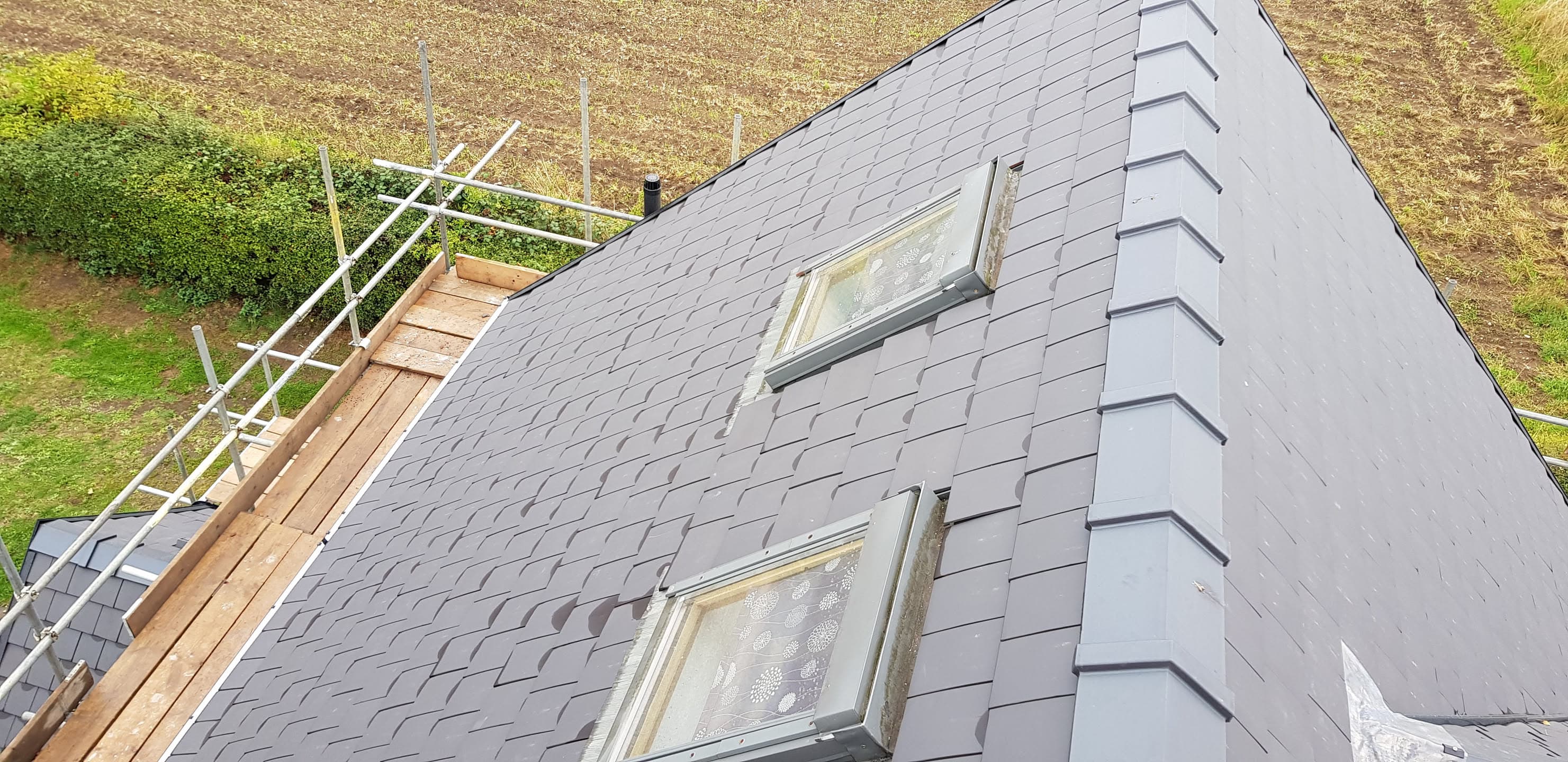 Pitched slate roof with two roof windows and grey ridge tiles