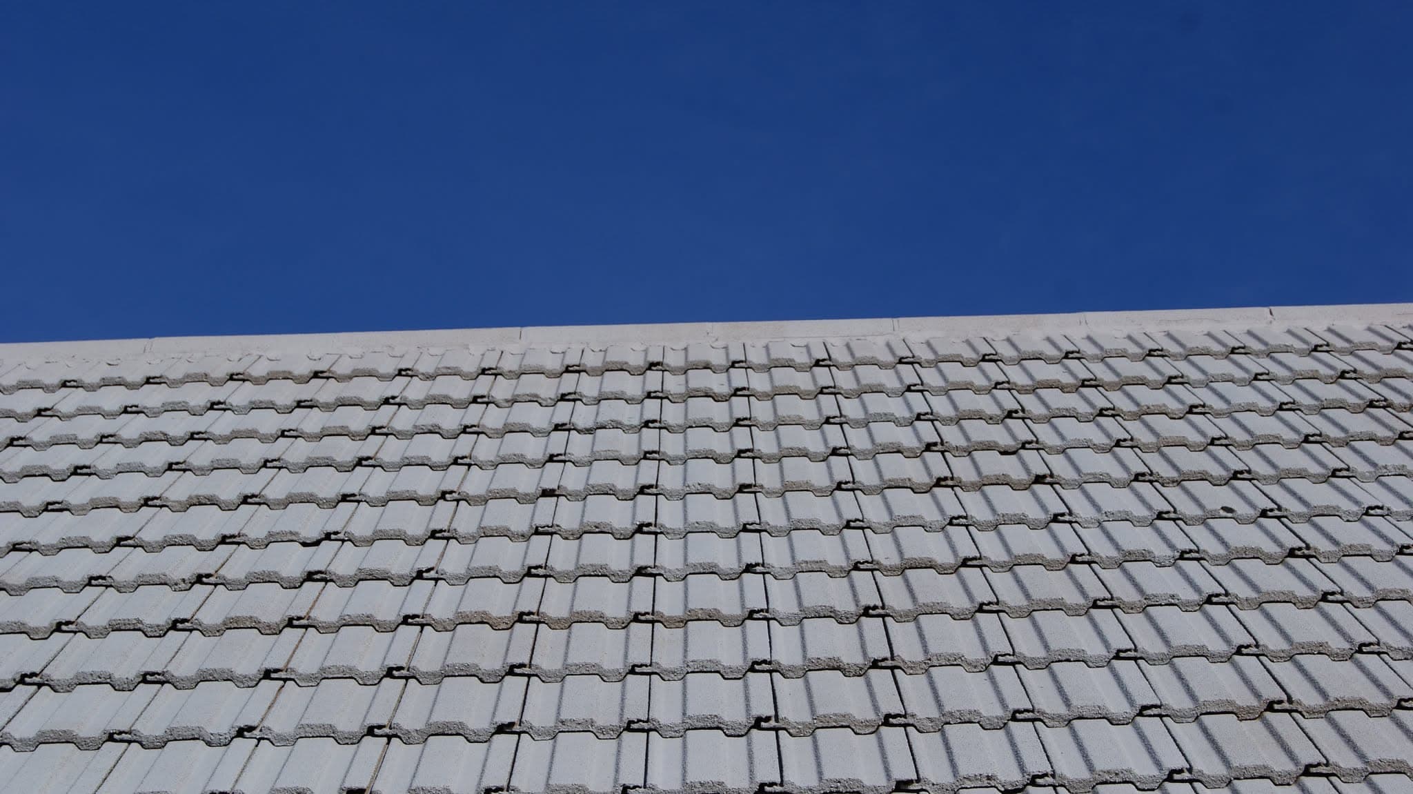 Pitched roof with grey concrete interlocking tiles against clear blue sky