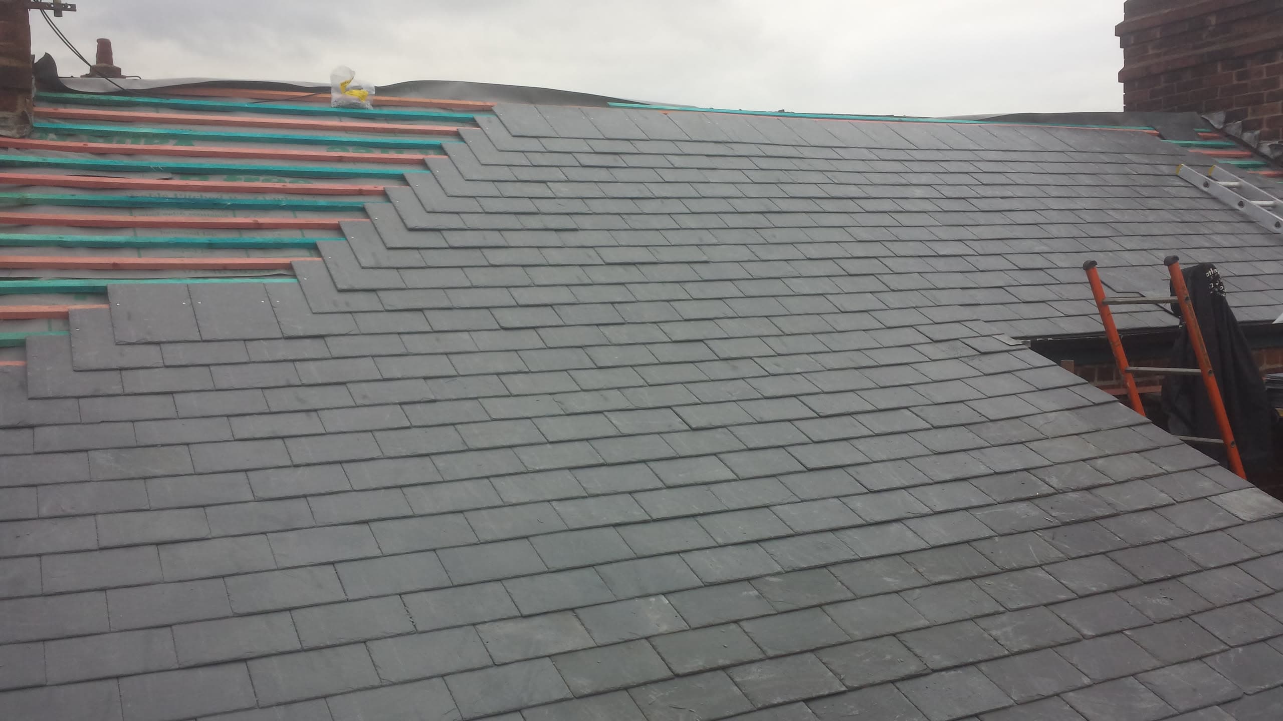 Grey slate pitched roof during installation with exposed battens and membrane visible