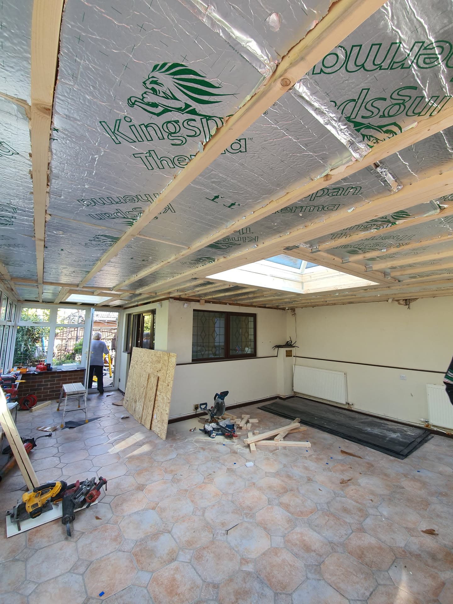 Conservatory roof installation in progress with insulation and timber framework visible, fitter working in background