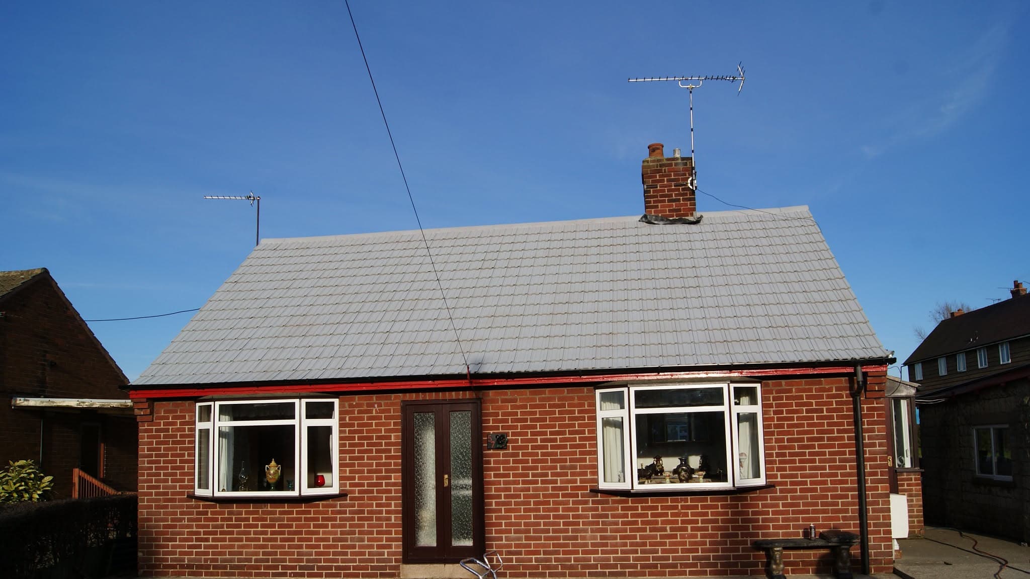 Pitched roof with light grey concrete tiles and brick chimney stack