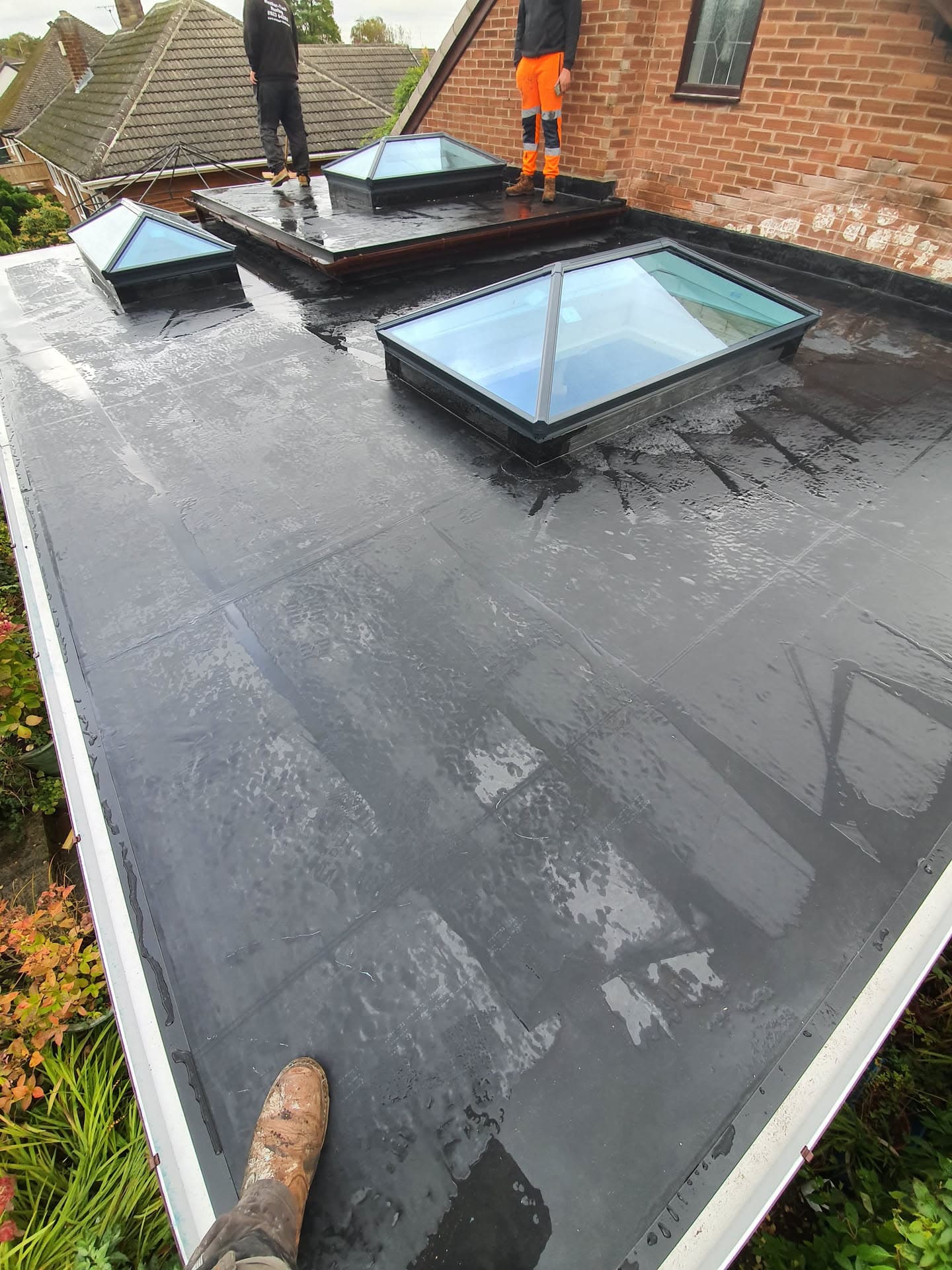 Flat roof with GRP fibreglass finish and three roof lanterns, fitter working in high-visibility trousers