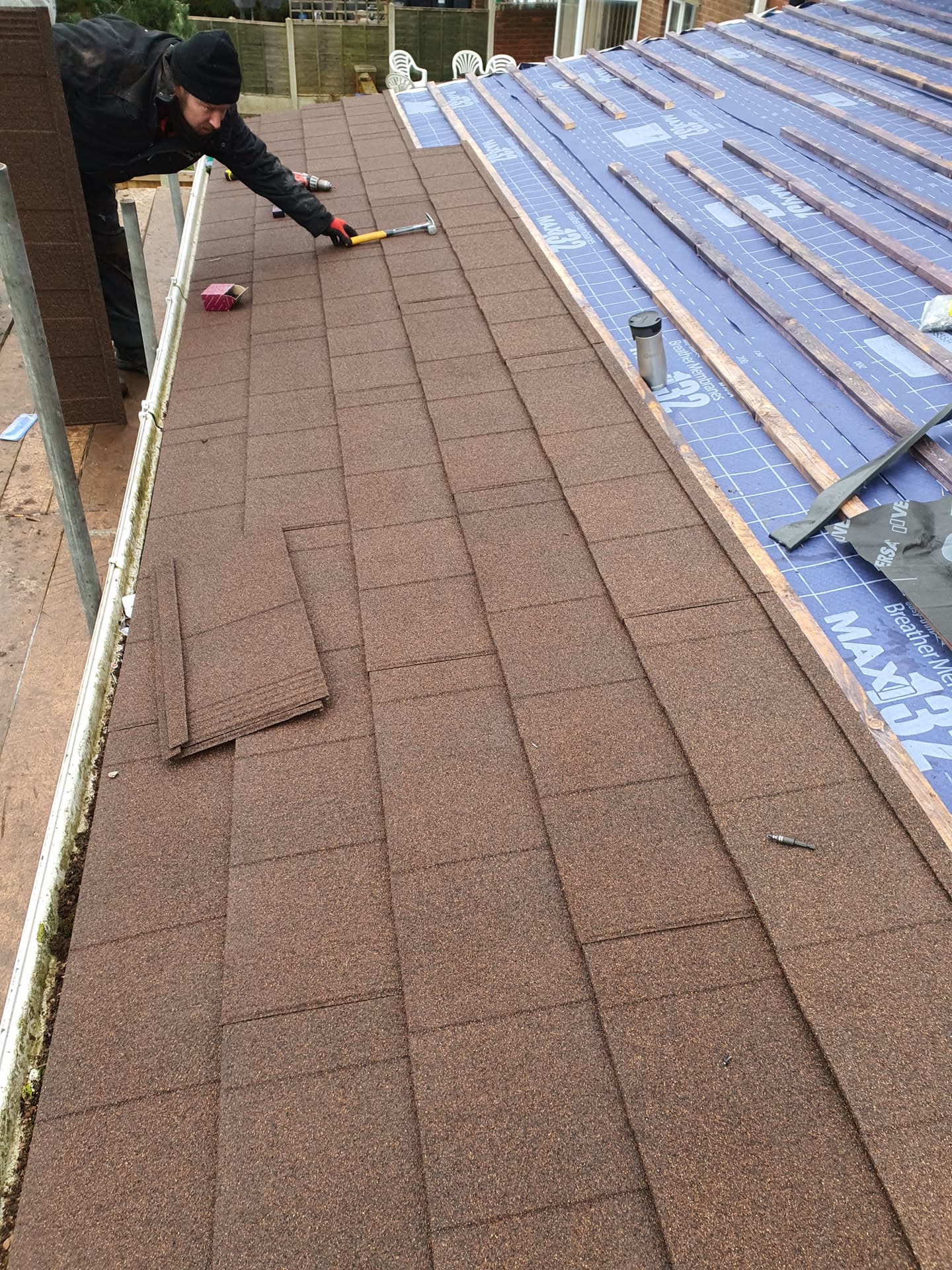 Fitter installing brown concrete tiles on pitched roof with blue membrane visible