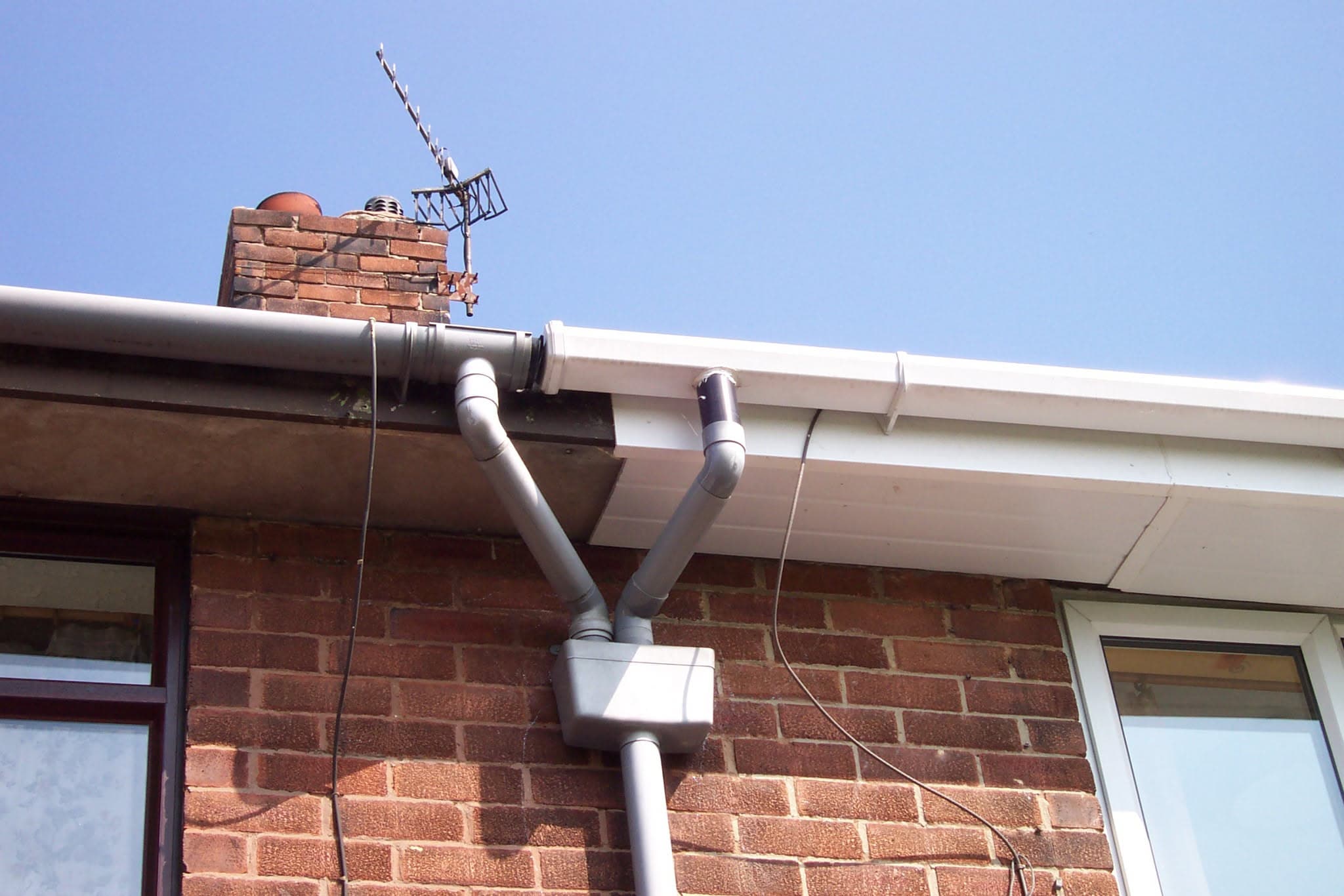 White fascia boards and grey guttering with downpipe on brick house with chimney stack