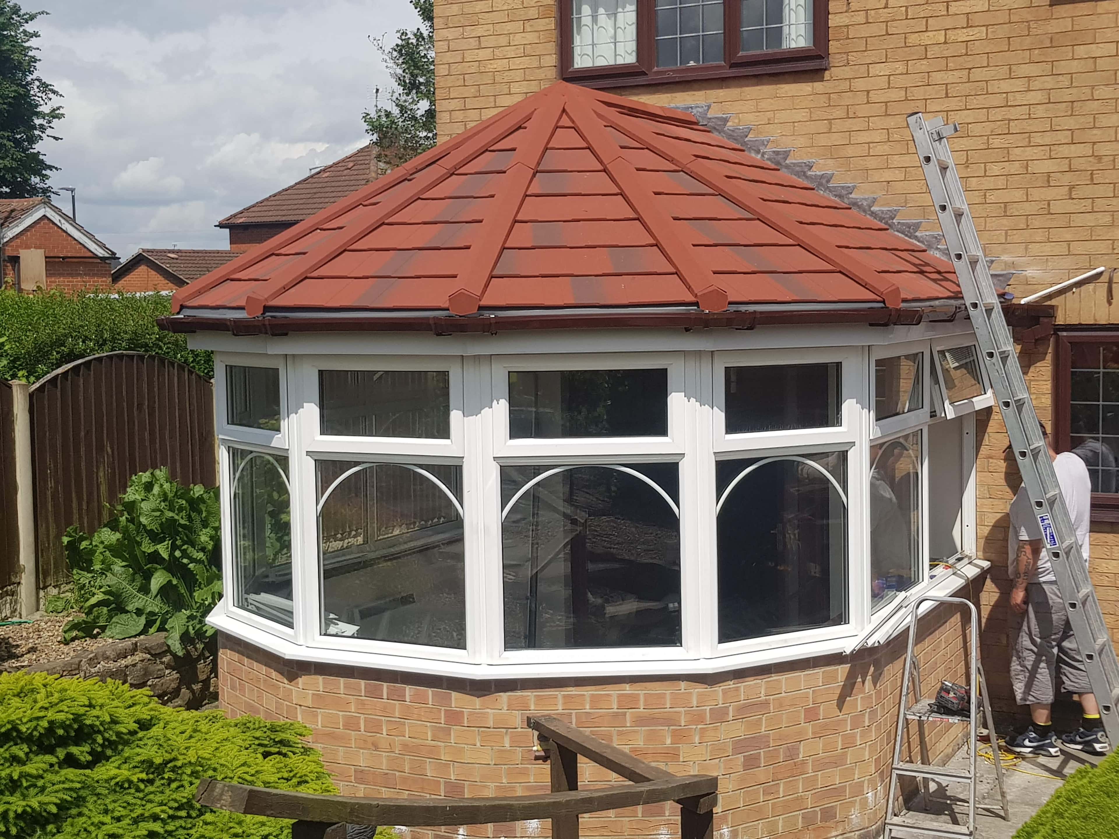 Newly installed red tiled conservatory roof with white uPVC frames and fitter working