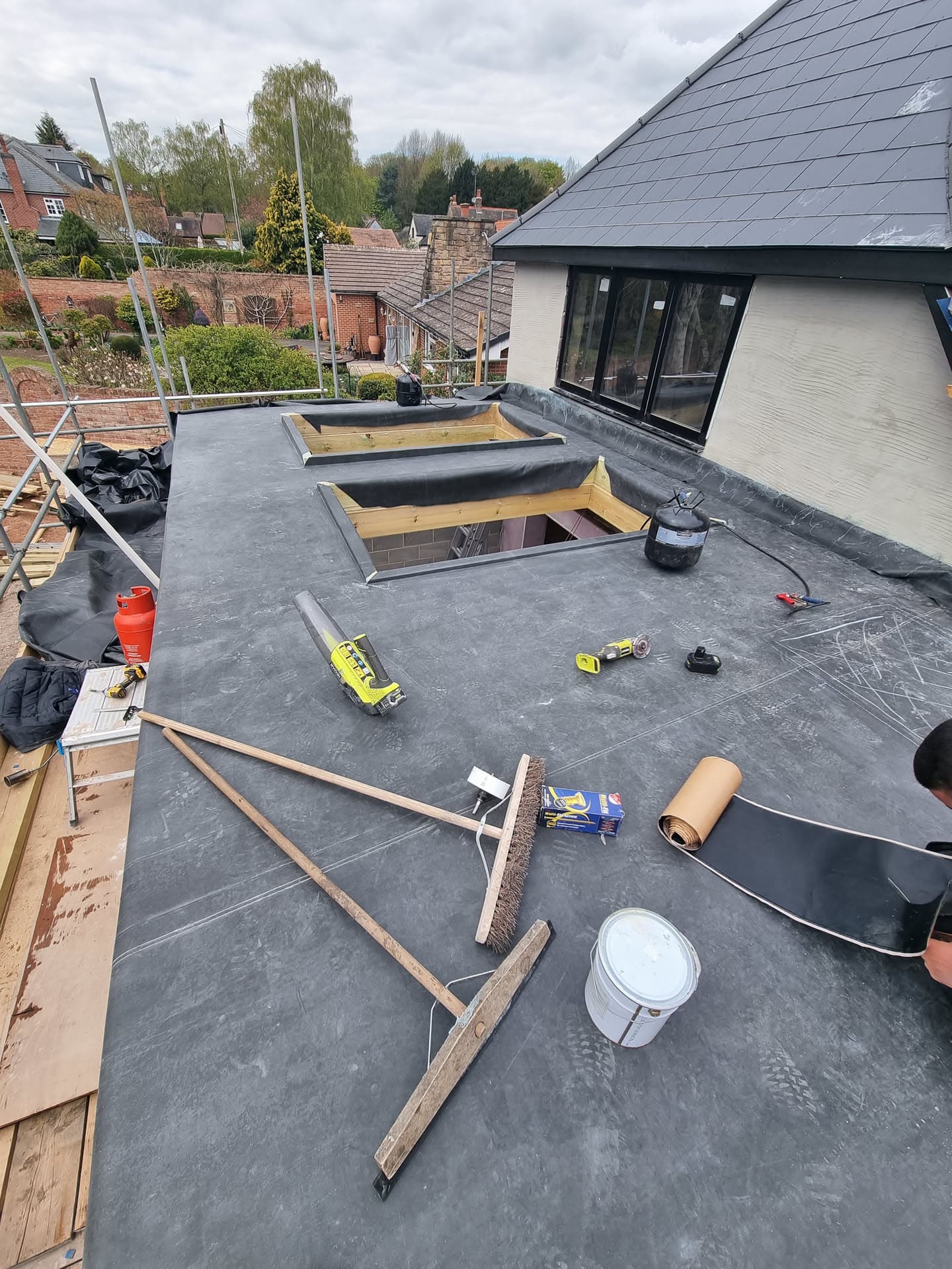 Flat roof installation in progress with felt membrane and timber-framed skylights