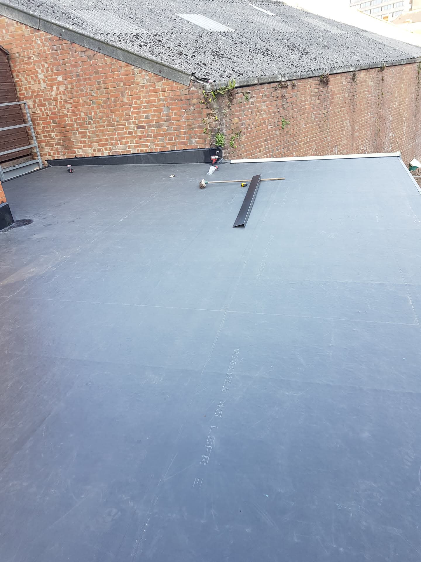Grey EPDM rubber flat roof installation in progress with fitter working near brick wall