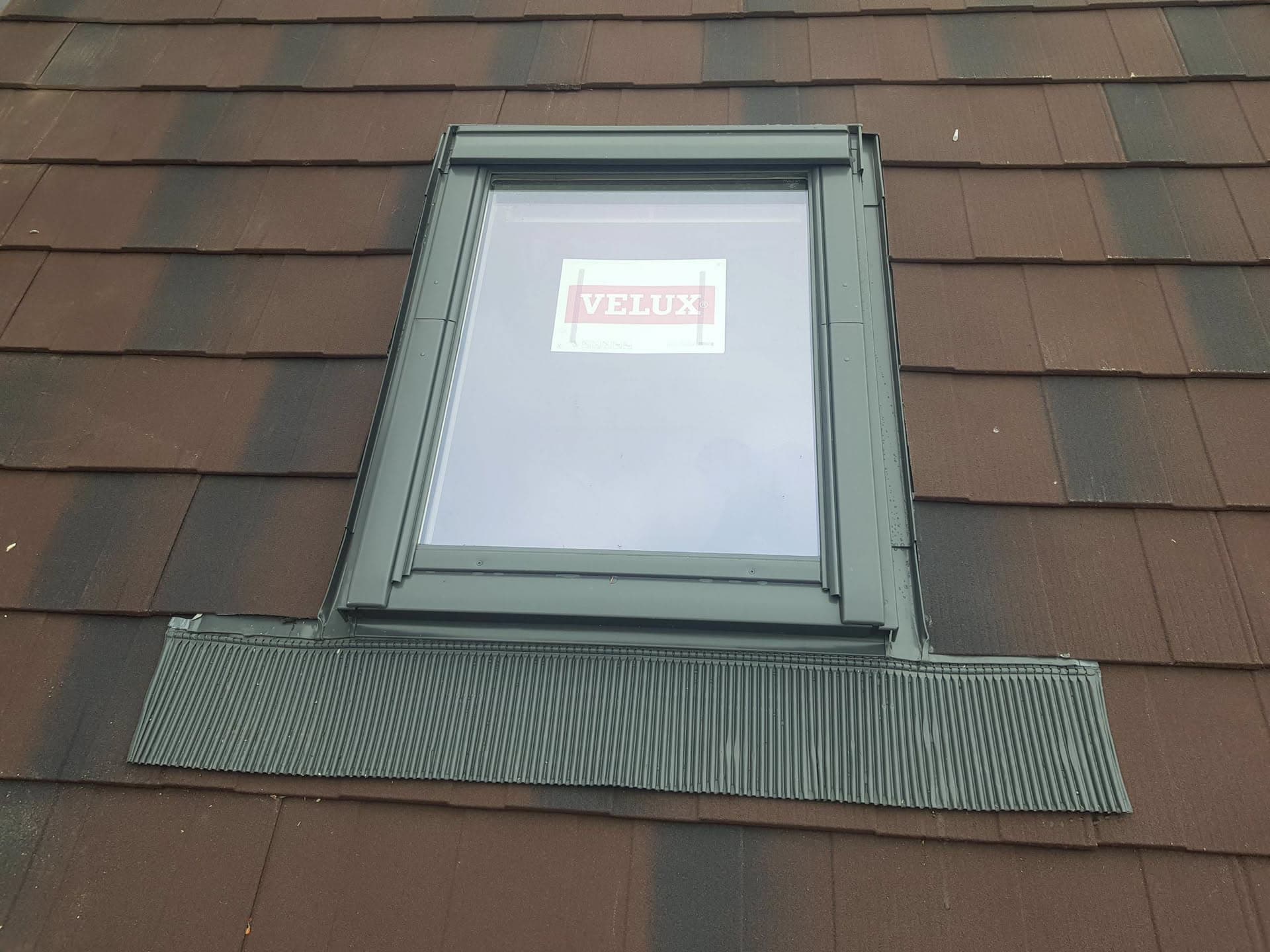 Velux roof window installed on brown tiled pitched roof with grey flashing