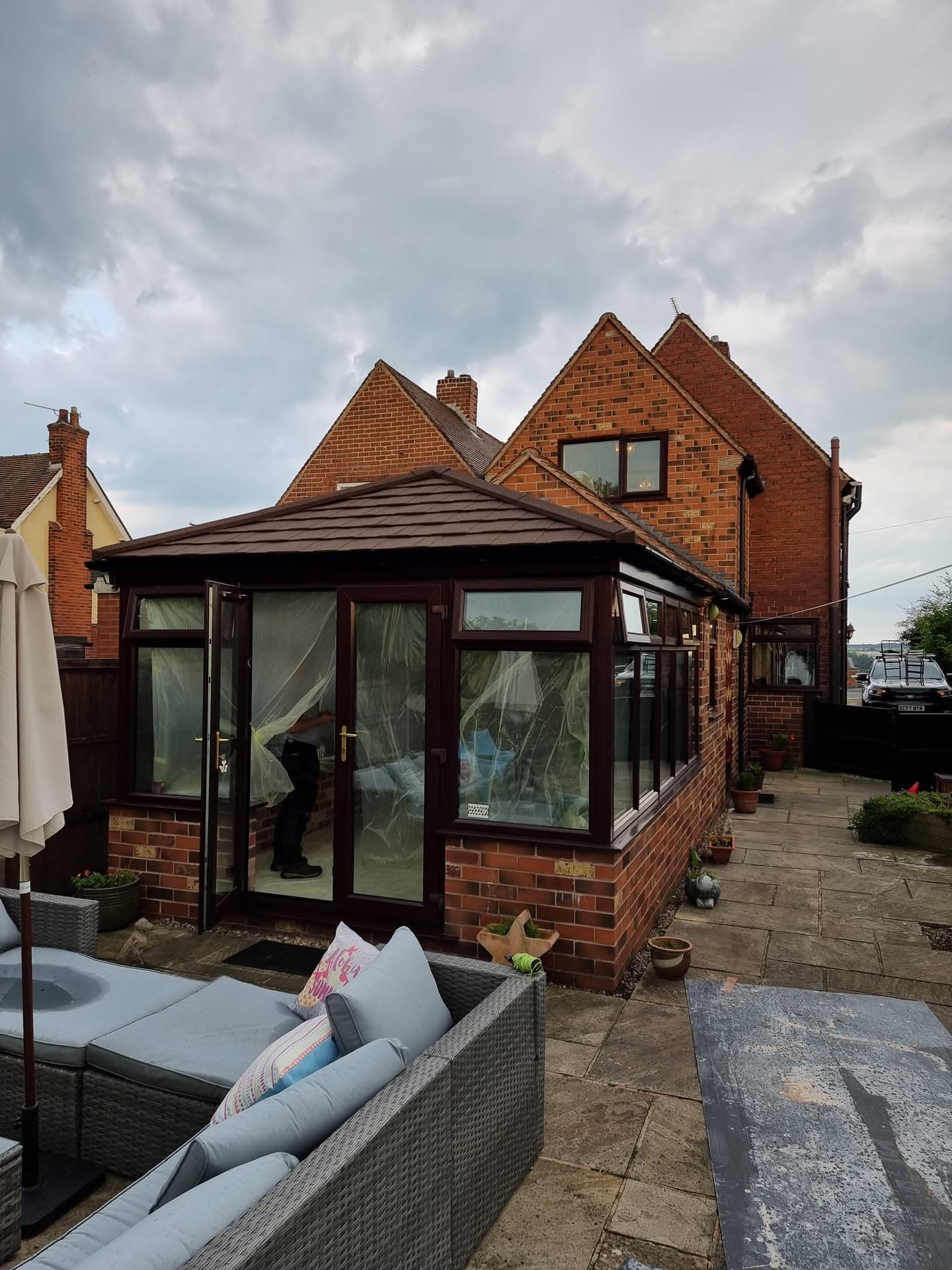 Conservatory with dark brown tiled roof and brick base attached to red brick house