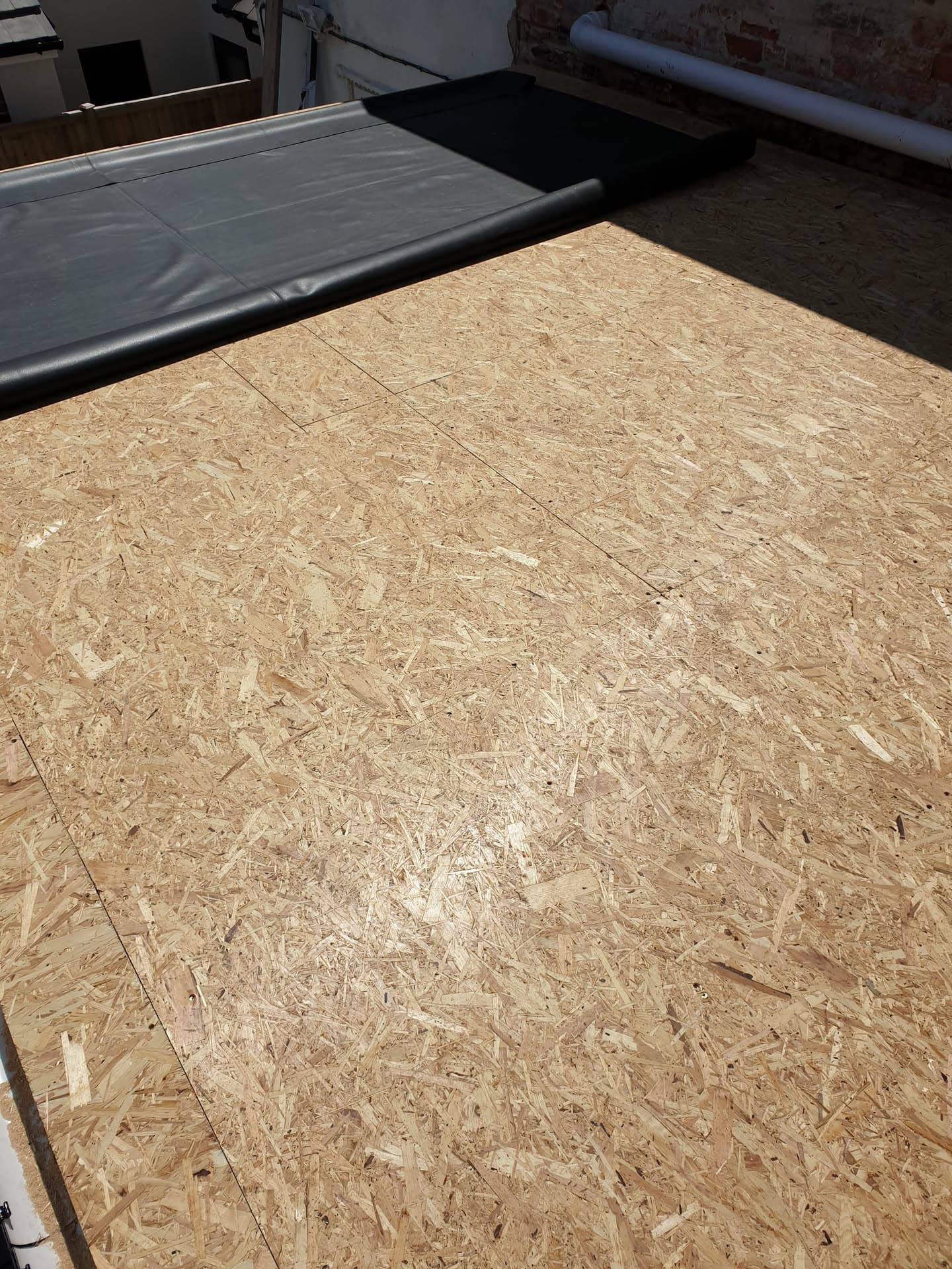 Flat roof with OSB boarding and black EPDM rubber membrane being installed