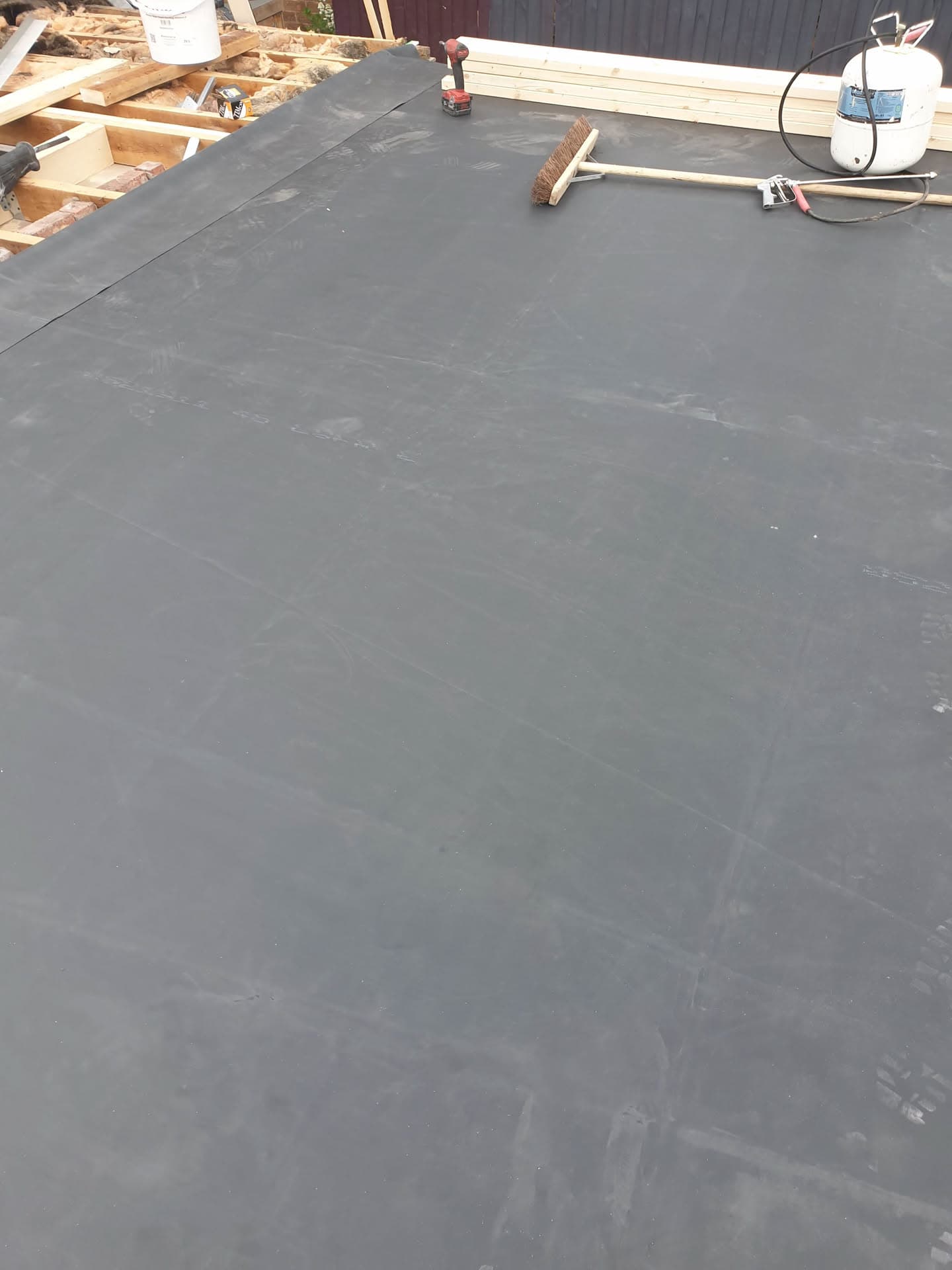 Flat roof covered with grey EPDM rubber membrane with brush and tools on surface