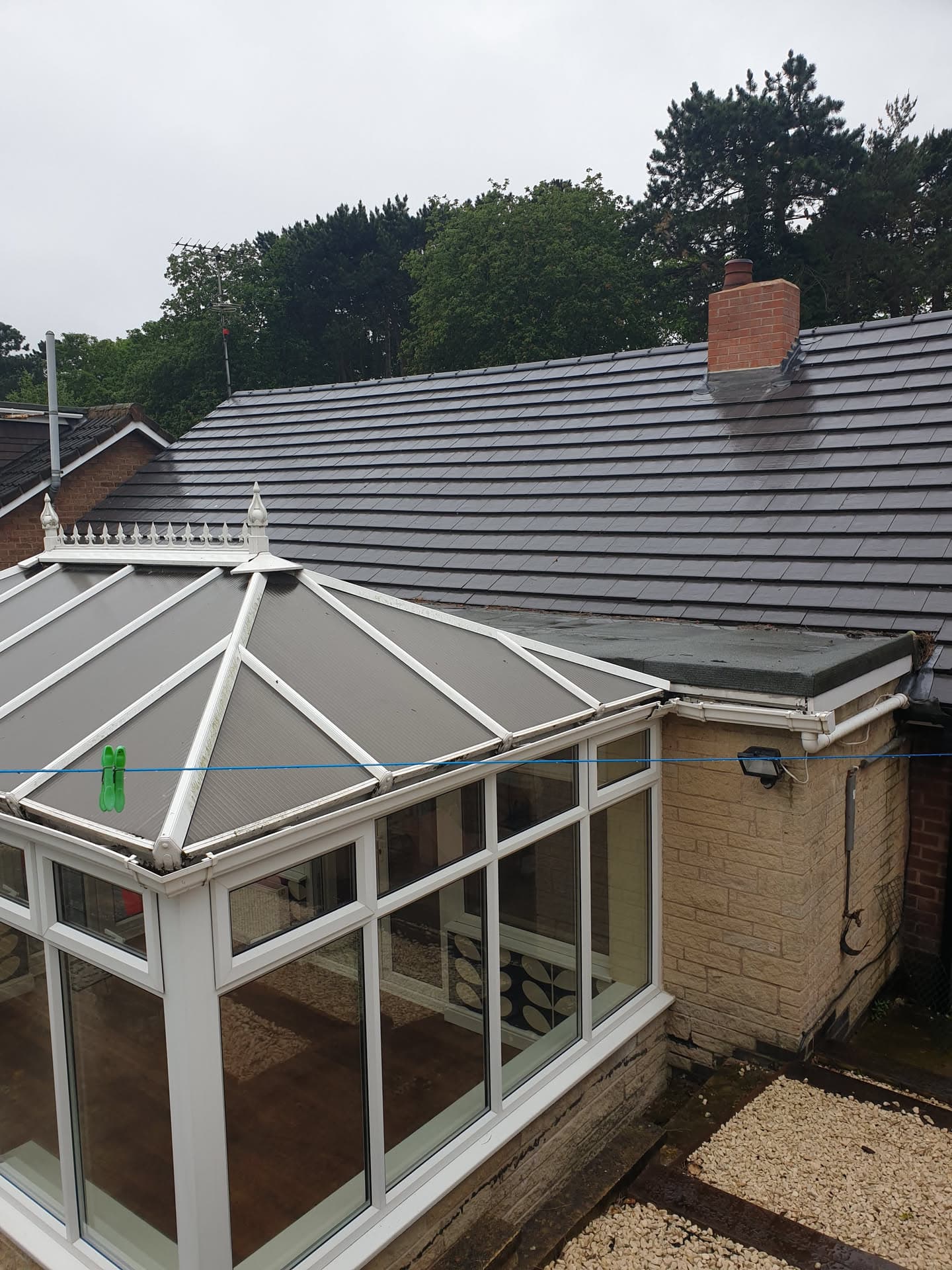 Pitched roof with grey concrete tiles and brick chimney, white uPVC conservatory below