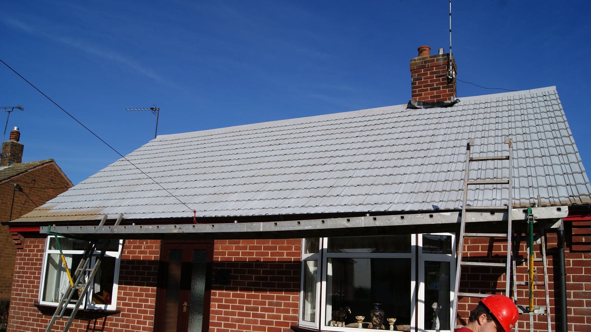 Pitched roof with grey concrete tiles and brick chimney stack, fascias and soffits visible