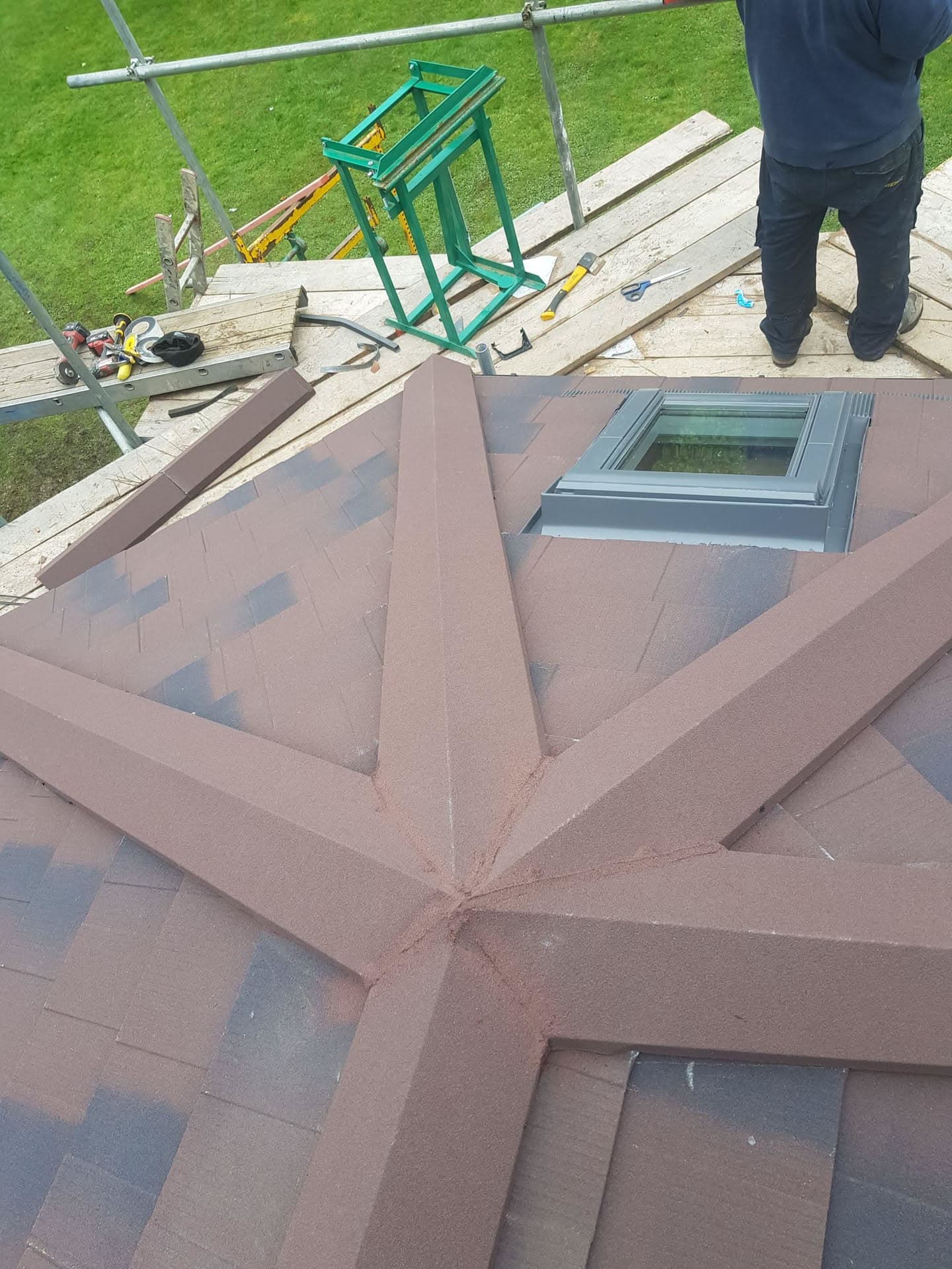 Pitched roof with brown concrete tiles and skylight window, fitter working with scaffolding visible