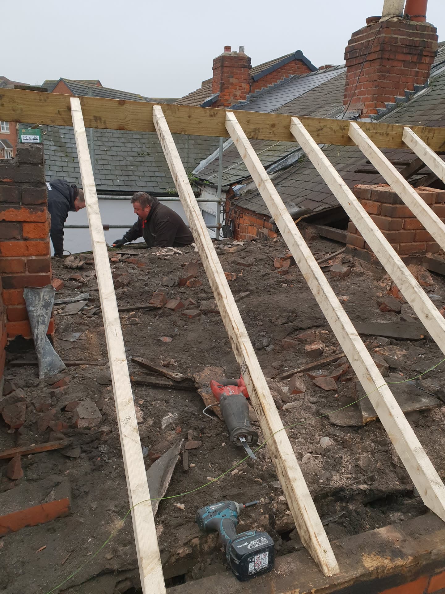 Fitters installing new timber roof joists on pitched roof with exposed brick chimney stacks