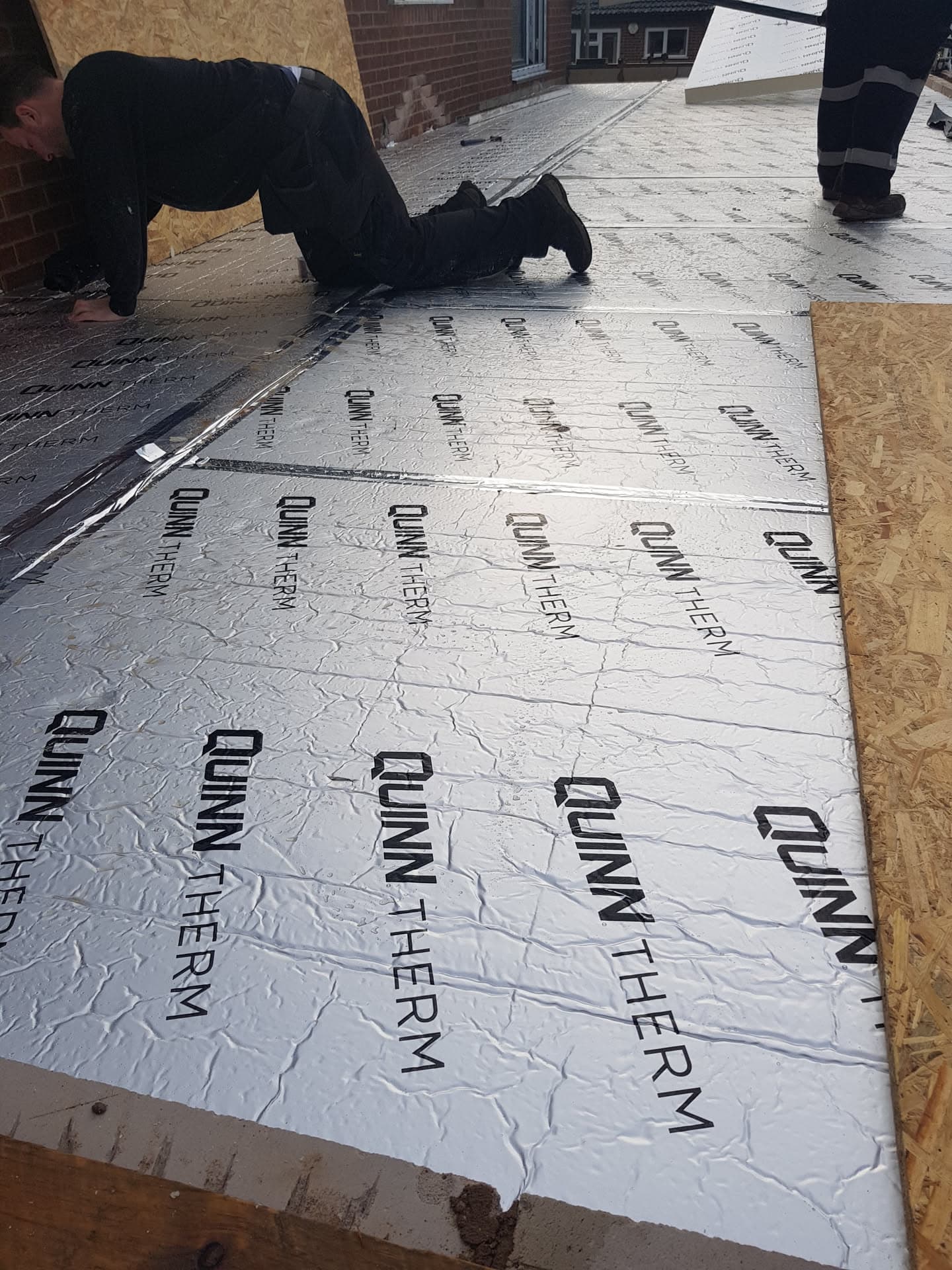 Fitter installing insulation boards on flat roof with OSB decking visible