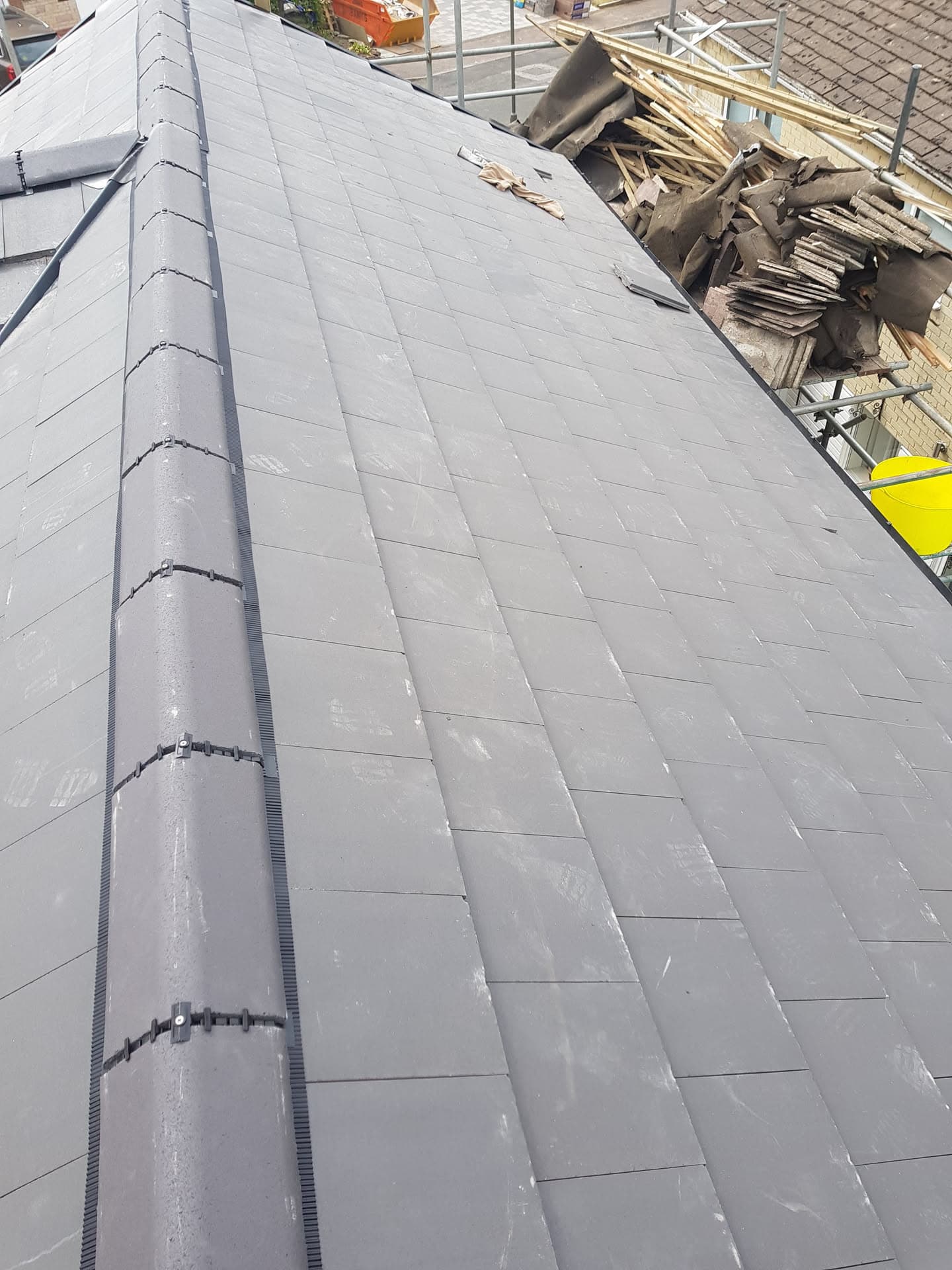 Newly completed grey tiled pitched roof with ridge tiles and scaffolding visible