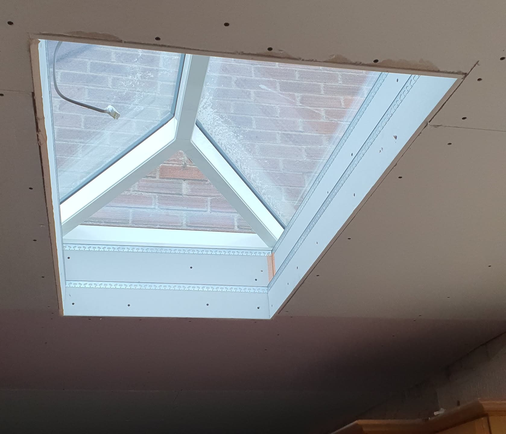 Roof window installation viewed from inside showing white frame and brickwork visible through glazing