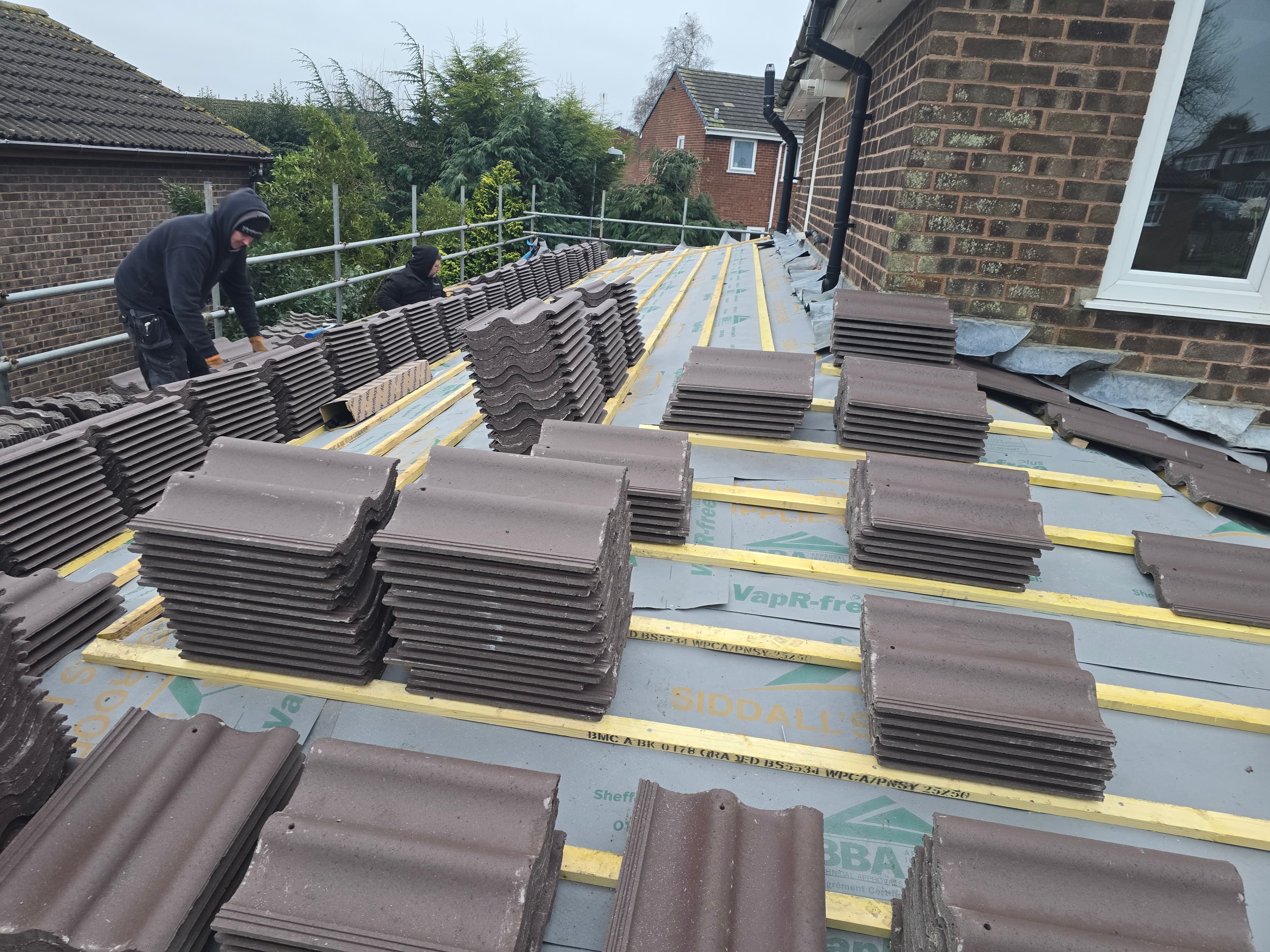 Roofers laying out brown concrete tiles across new battens and breathable membrane during a re-roof
