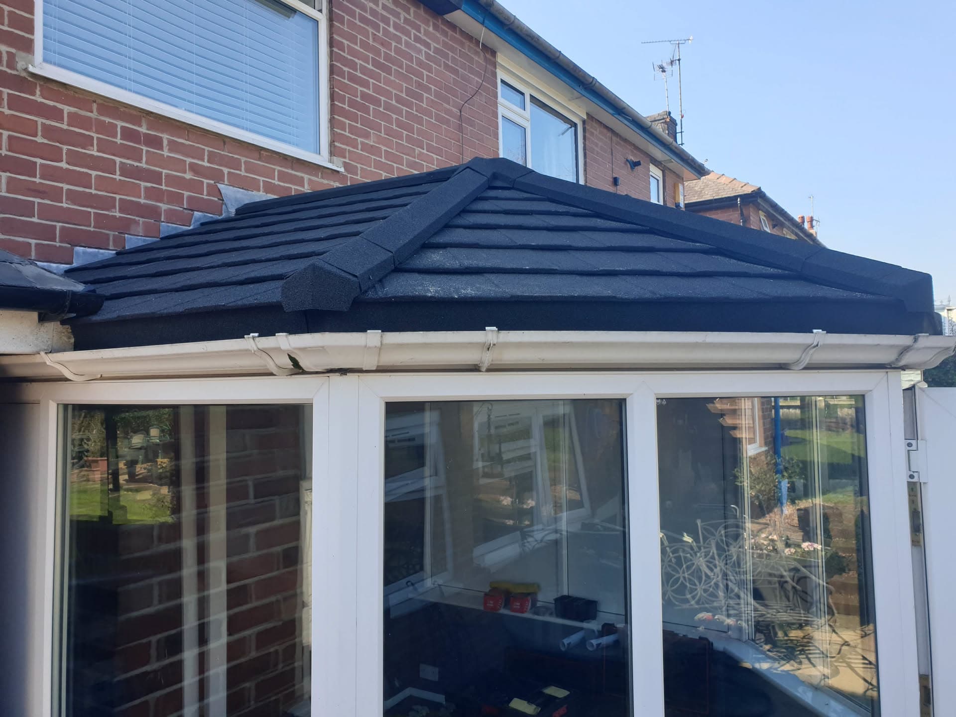 Conservatory with dark grey tiled roof and white fascias and guttering