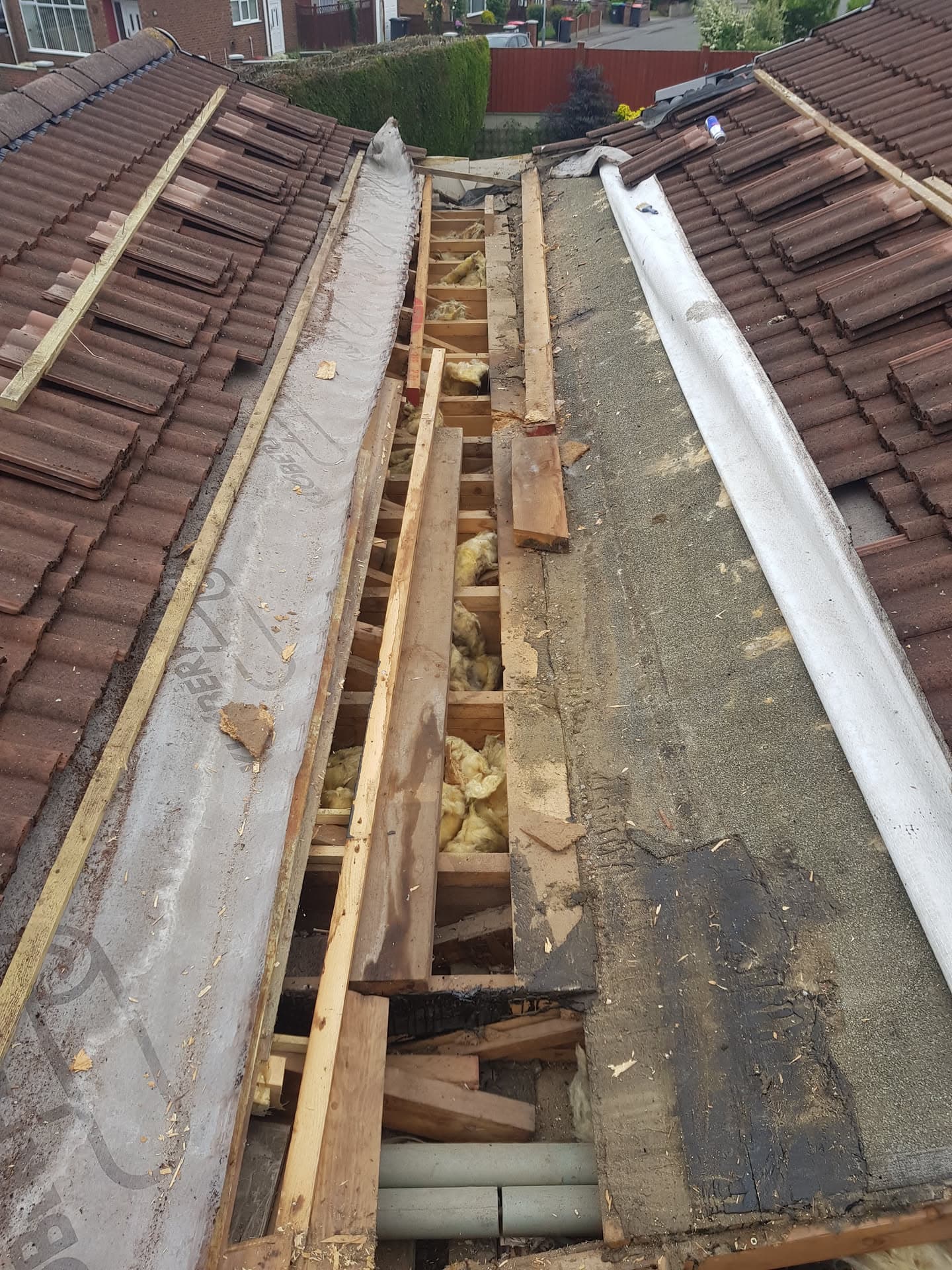 Pitched roof valley repair in progress showing exposed timber joists, insulation and brown concrete tiles