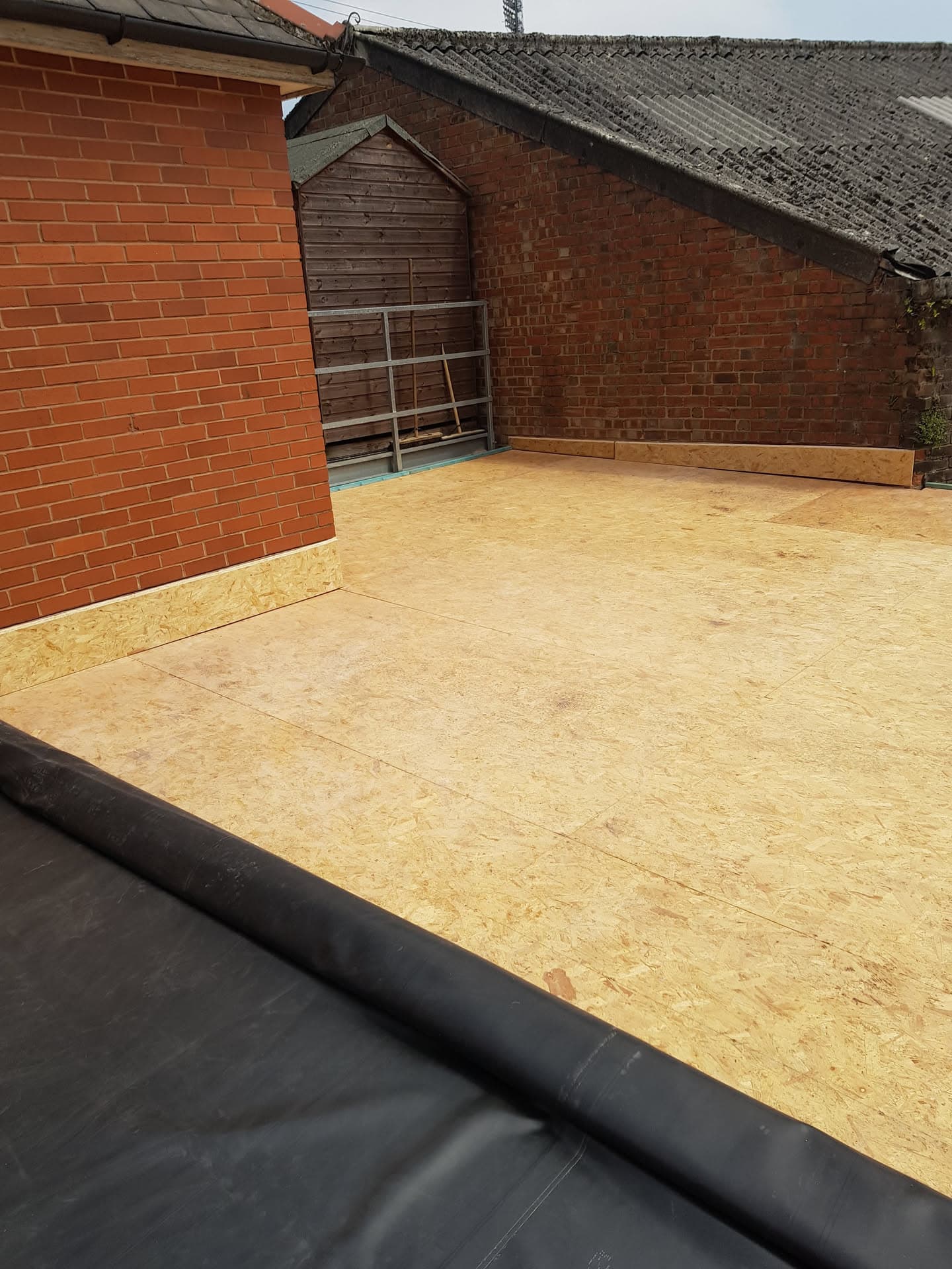 New flat roof installation with OSB decking and EPDM rubber membrane on brick building