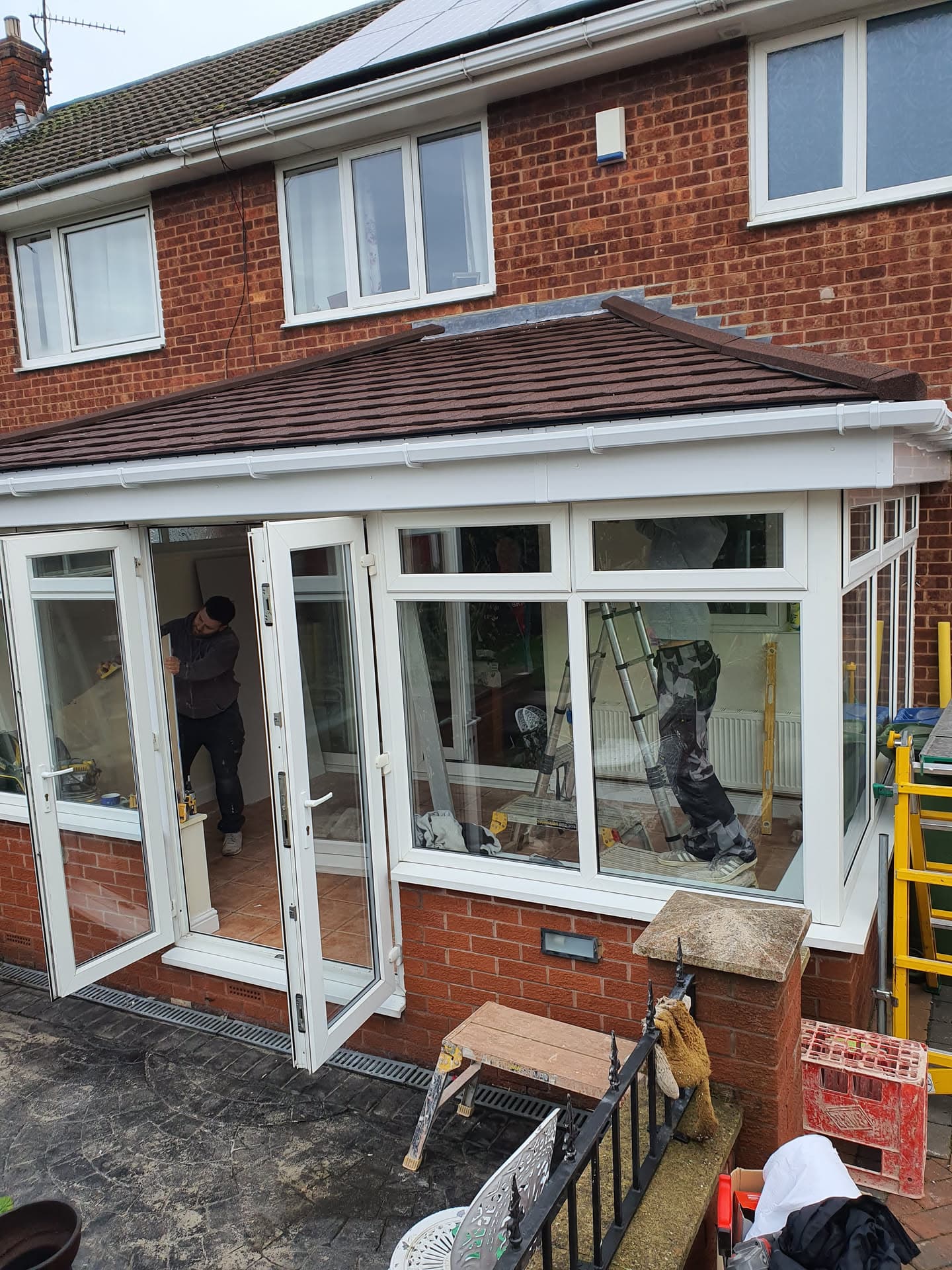 Brown tiled conservatory roof with white fascias and guttering, fitters working inside