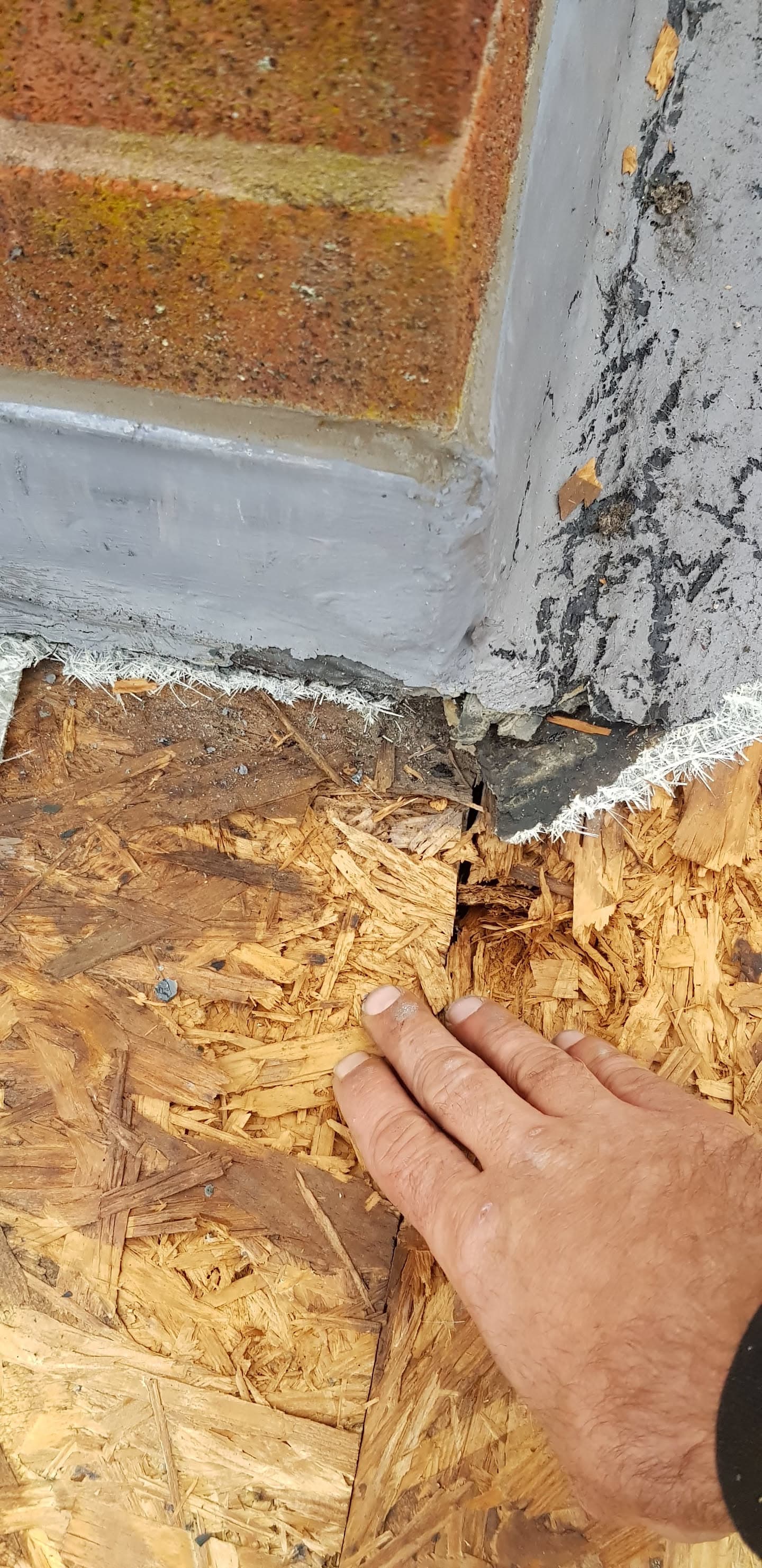 Fitter's hand inspecting white painted fascia board junction with OSB decking and brick wall