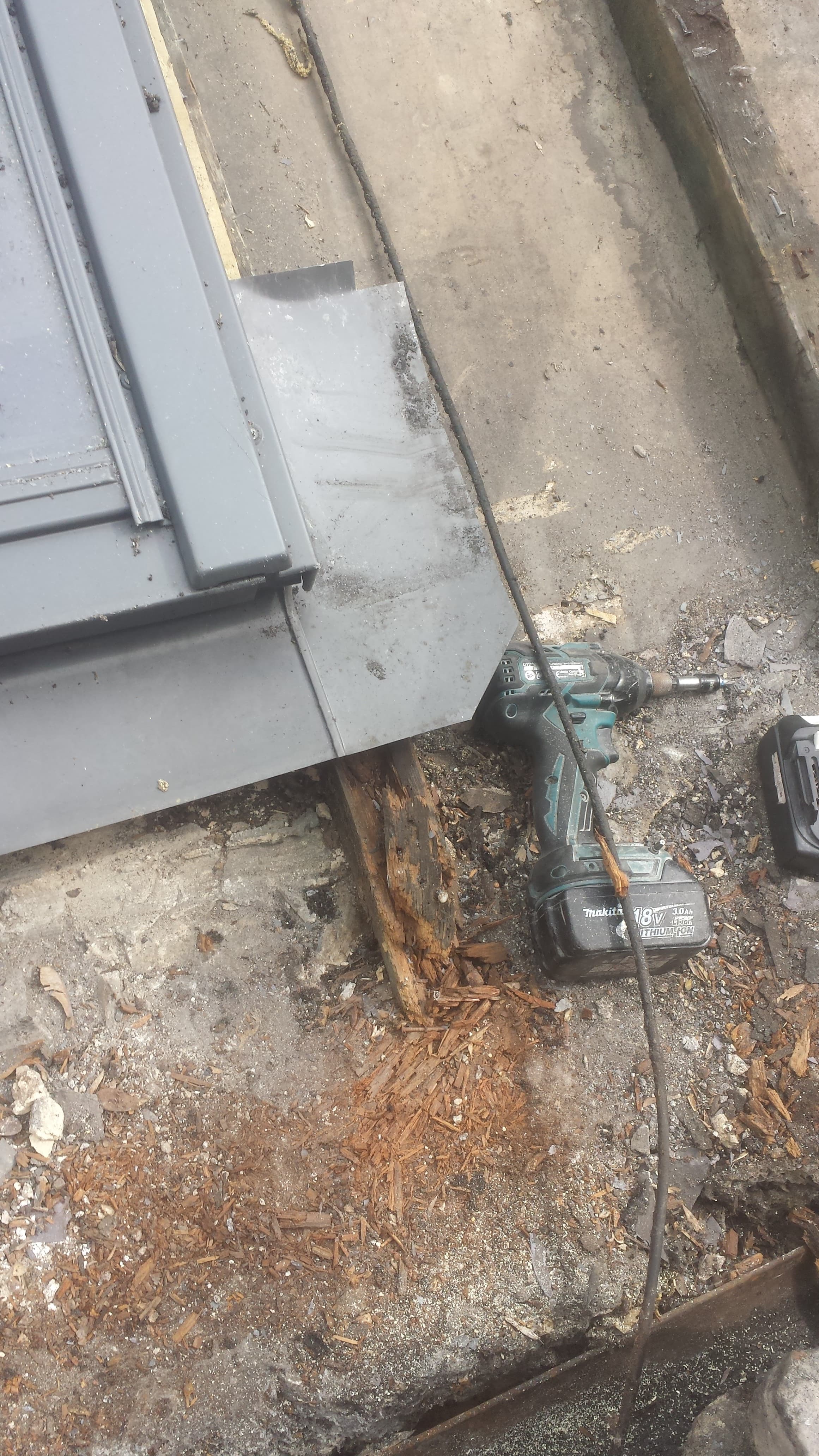 Flat roof repair work in progress with power drill and materials on weathered roof surface