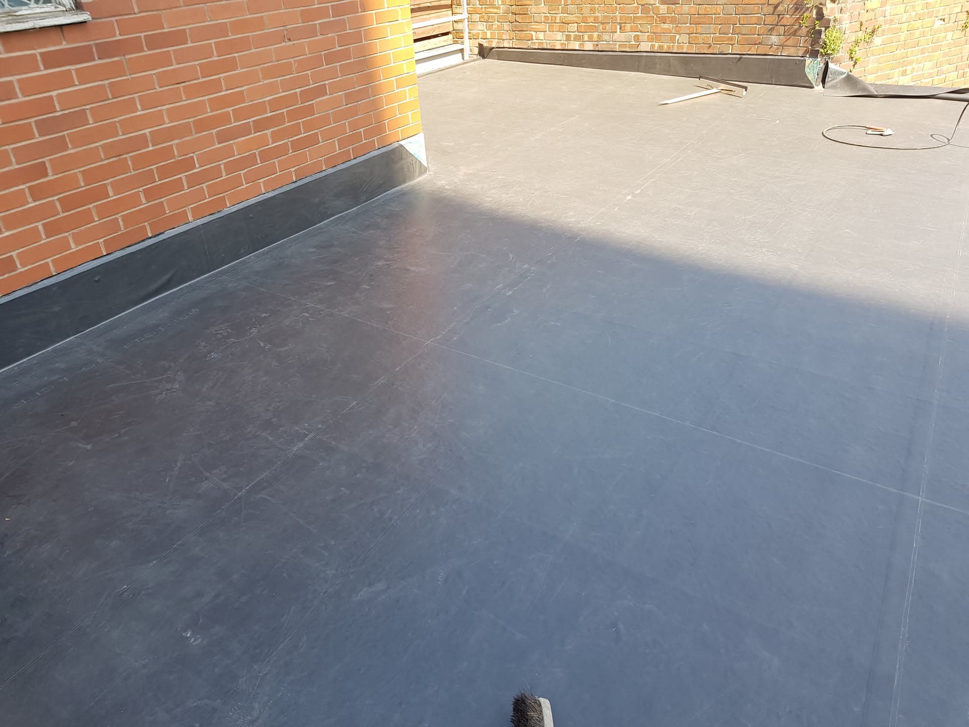 Grey EPDM rubber flat roof with dark flashing against brick walls