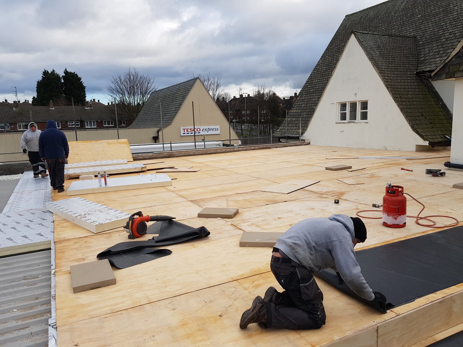 Fitters installing plywood decking and EPDM rubber membrane on a large flat roof