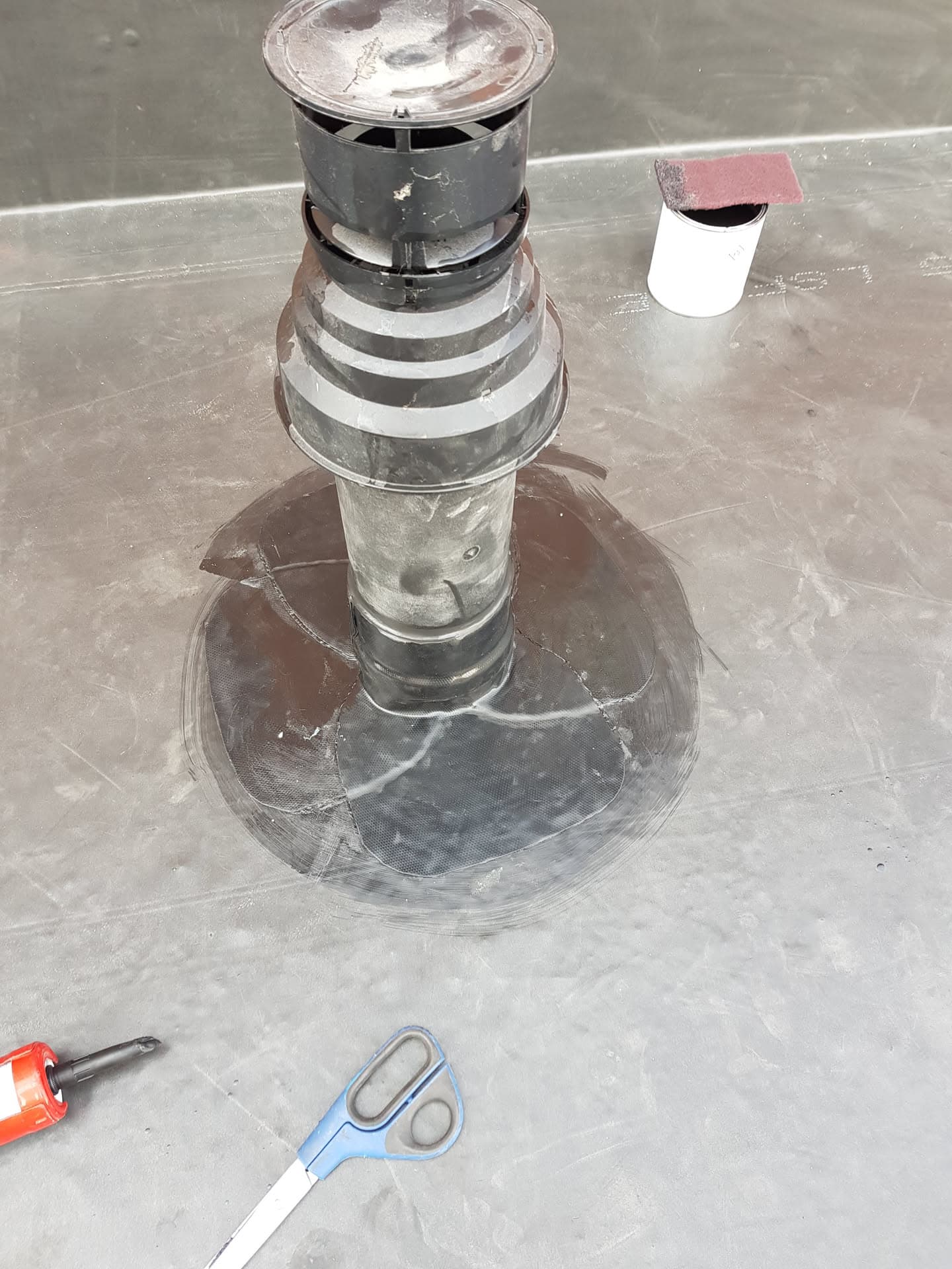 Metal flue terminal with rain cowl installed on grey flat roof membrane