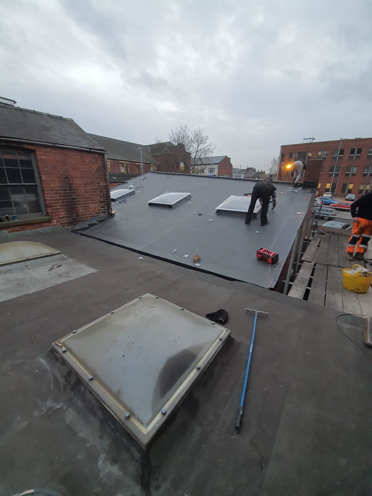 Fitter installing dark grey EPDM rubber flat roof with skylights on commercial building