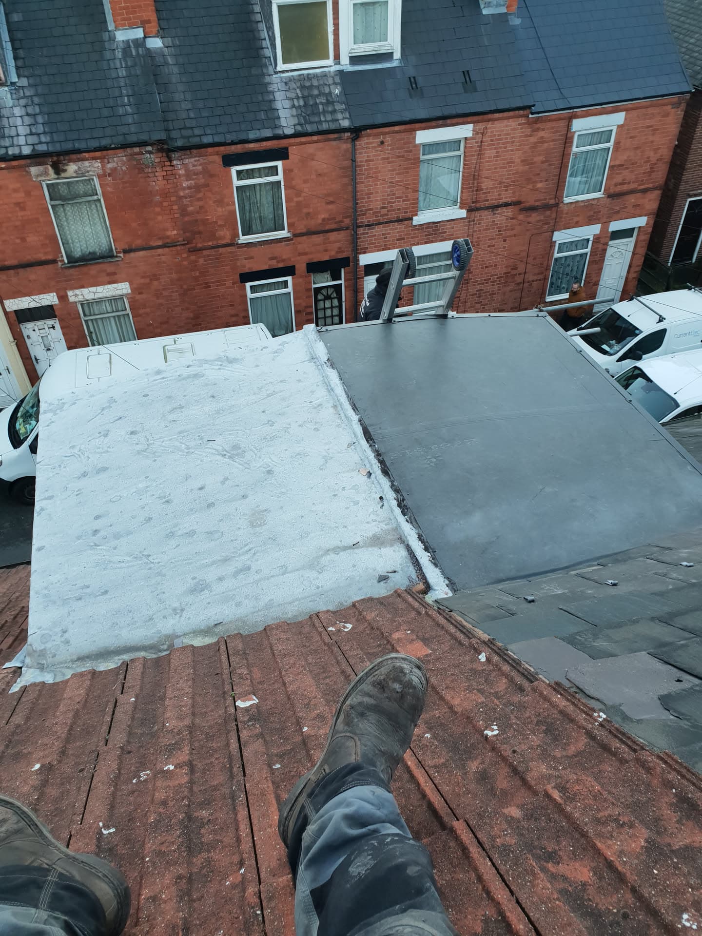 Flat roof installation in progress showing grey EPDM rubber membrane and white felt sections on terraced house extension