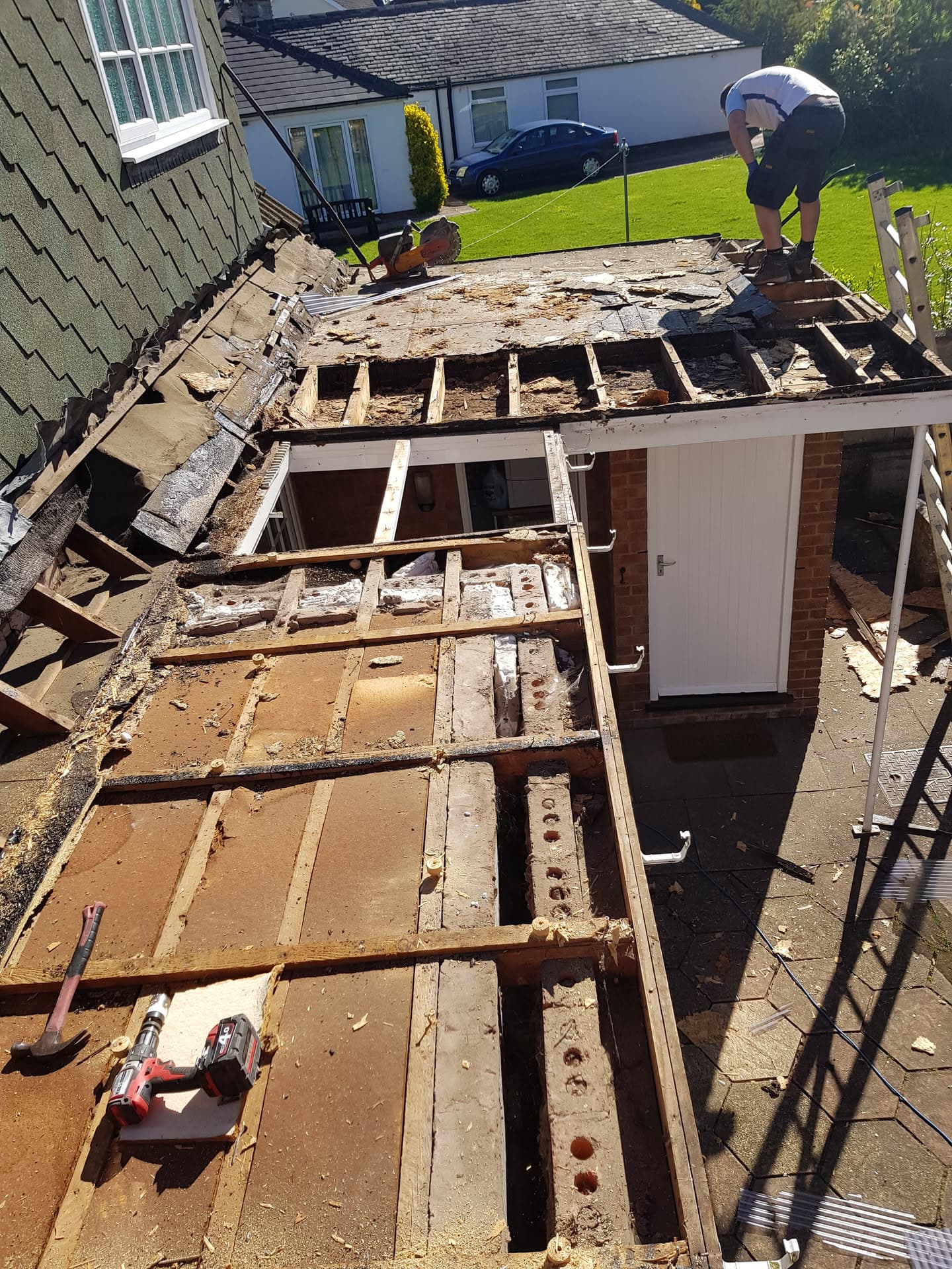 Flat roof replacement in progress with exposed timber joists and fitters working on decking