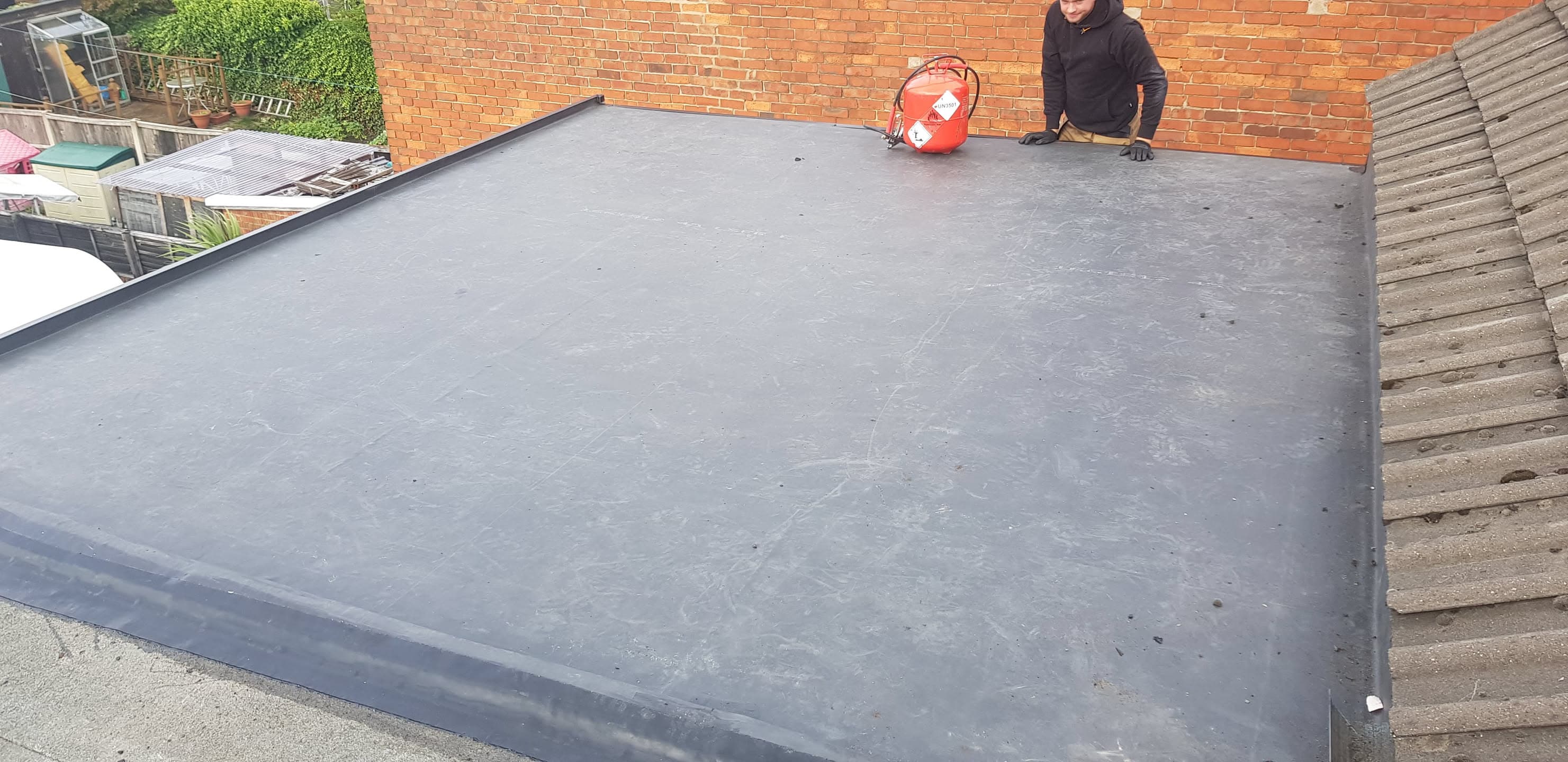 Fitter working on grey flat roof extension with adjacent tiled pitched roof