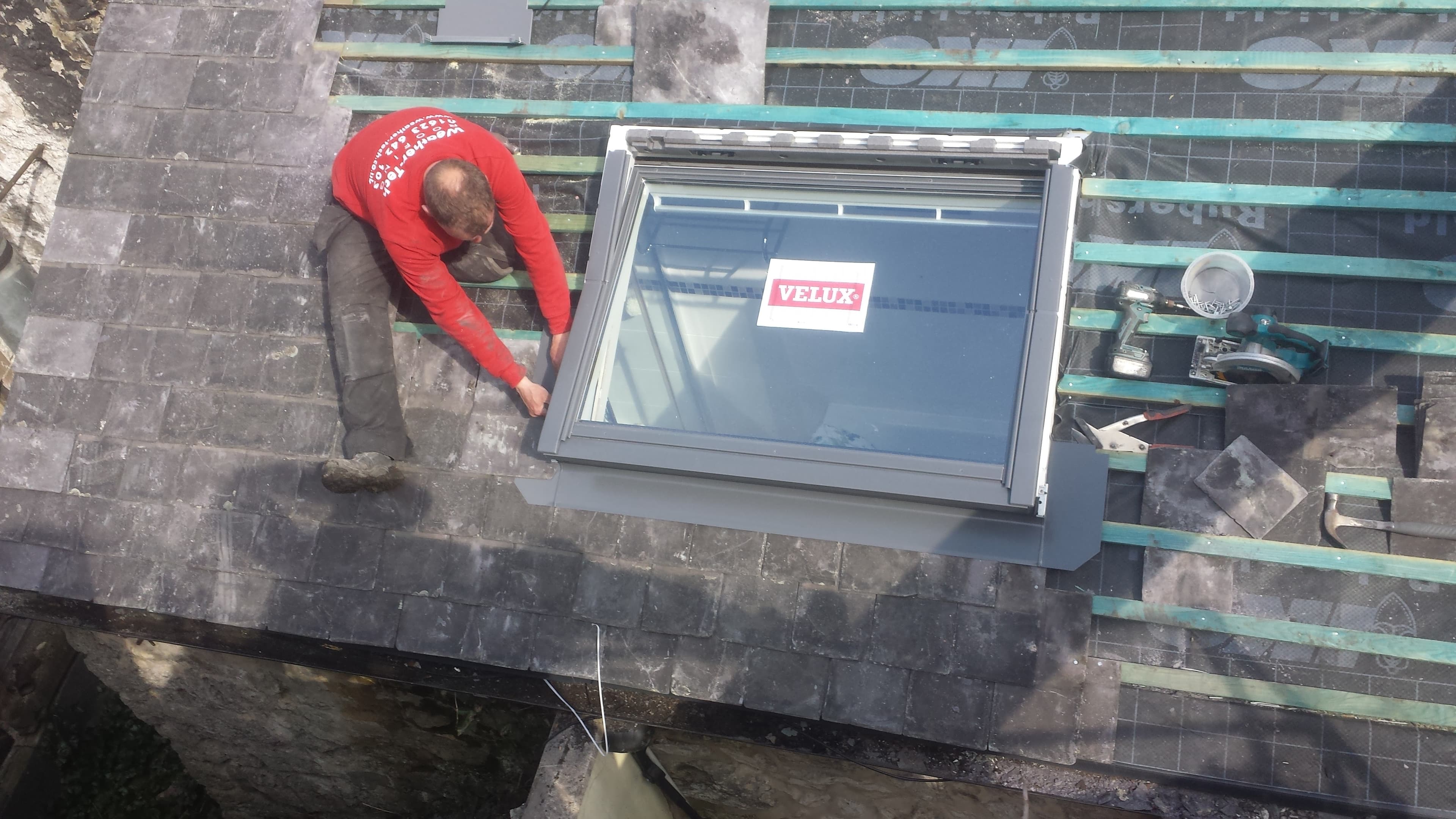 Fitter installing Velux roof window on dark slate pitched roof