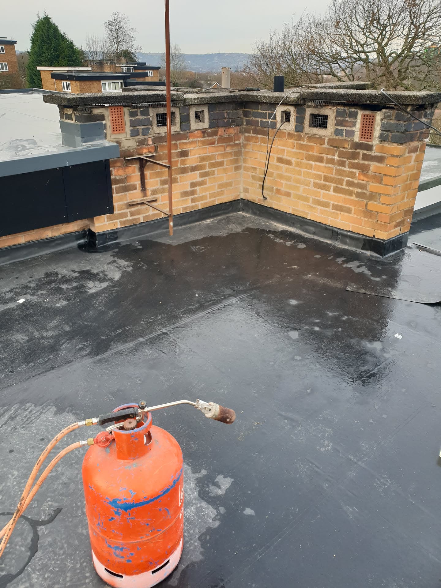 Flat roof with dark felt surface and brick chimney stack with lead flashing