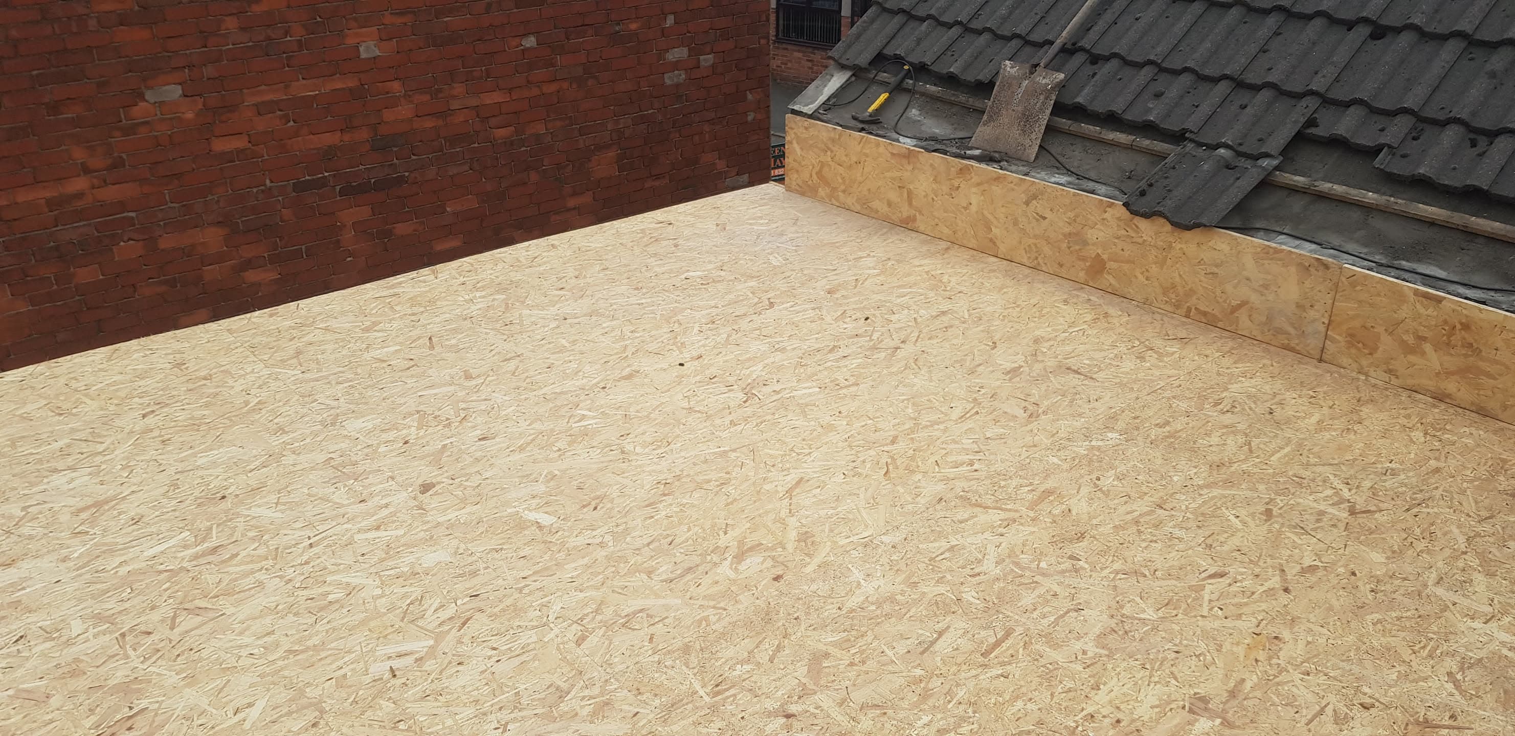 Flat roof with new OSB decking installed against brick wall and adjacent tiled roof