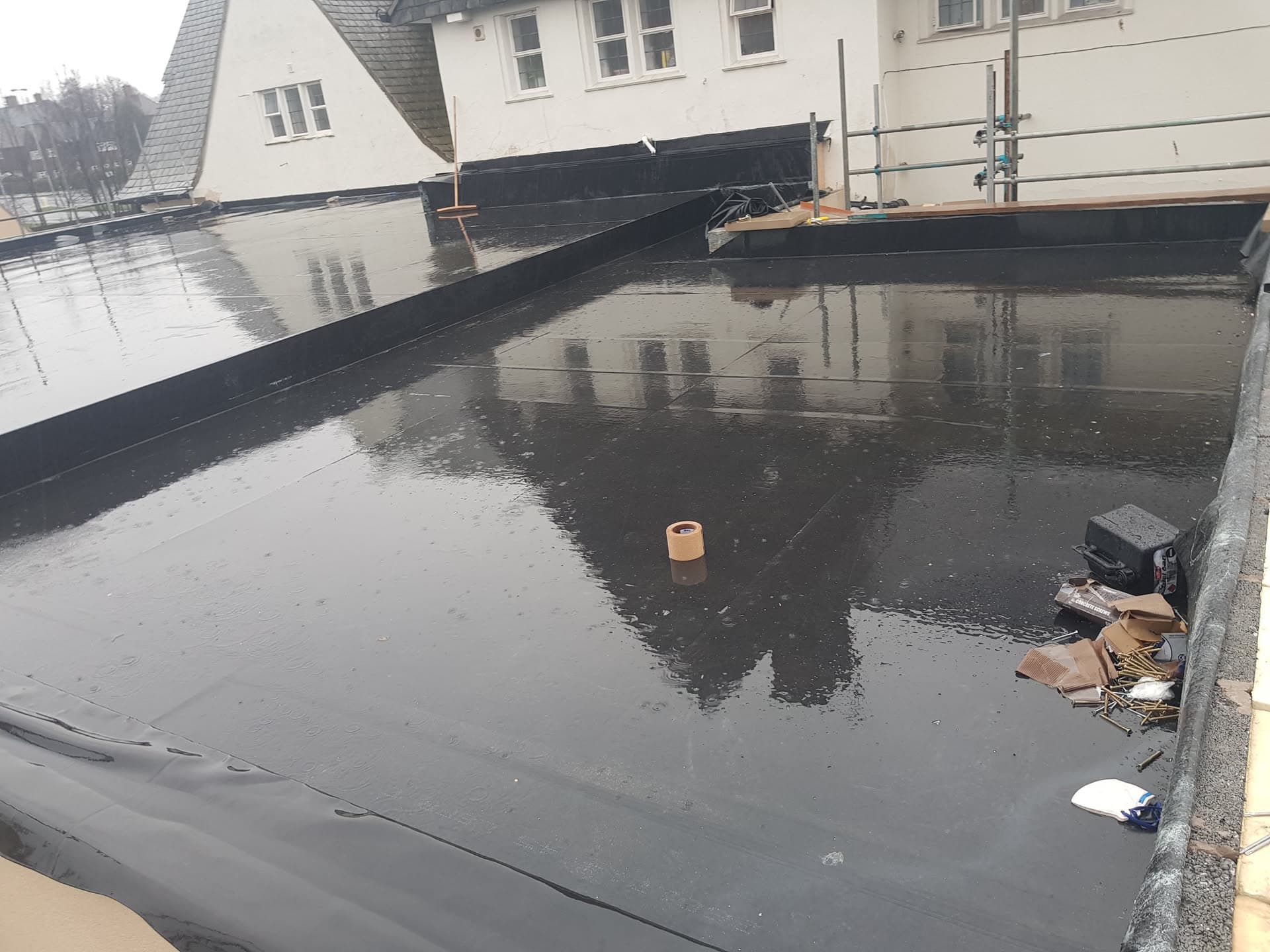 Newly installed black GRP fibreglass flat roof with reflective wet surface and scaffolding