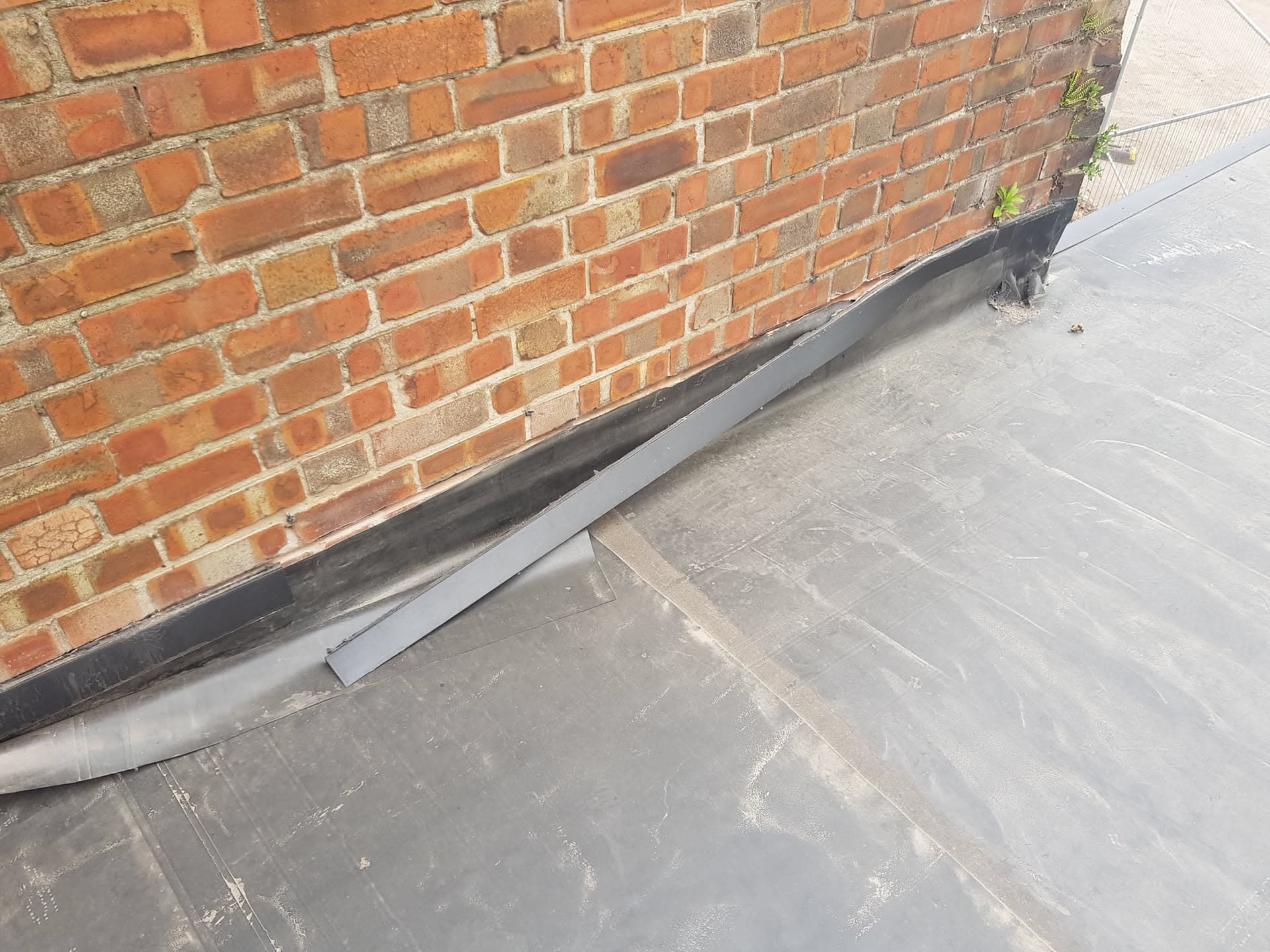 Grey flat roof with lead flashing against red brick wall