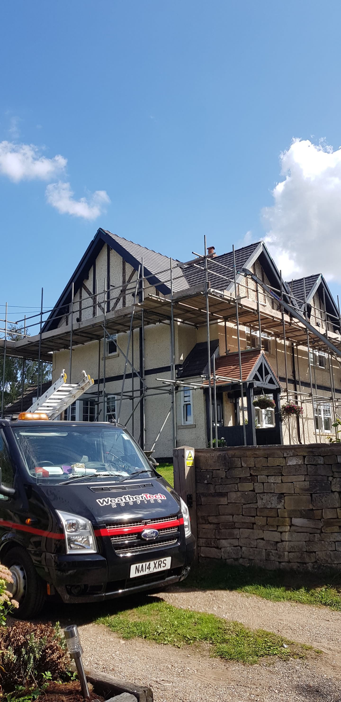 Pitched tiled roof with scaffolding on Tudor-style house with WeatherTech van parked outside