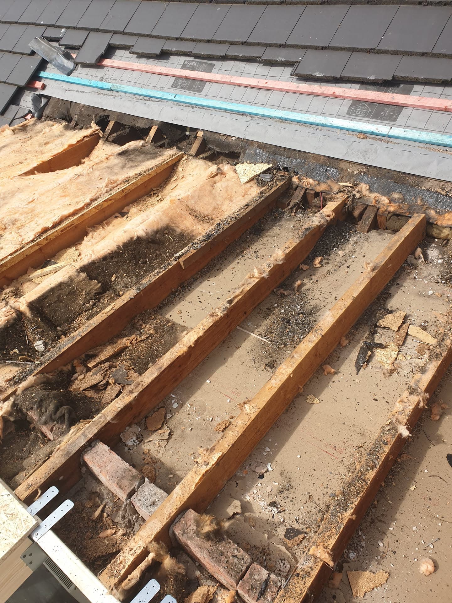 Exposed roof joists and insulation during flat roof repair with grey slate tiles visible above