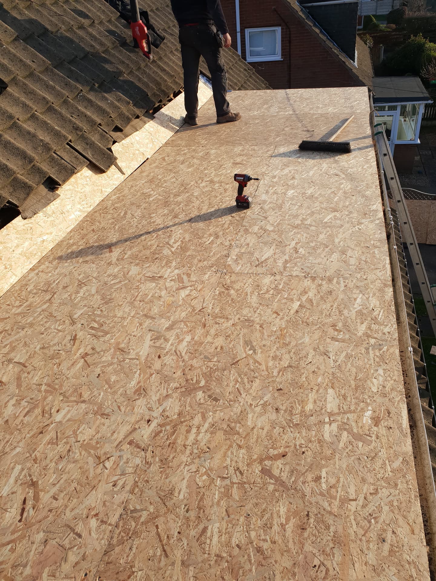 Fitter installing OSB boarding on flat roof extension with tiled pitched roof visible