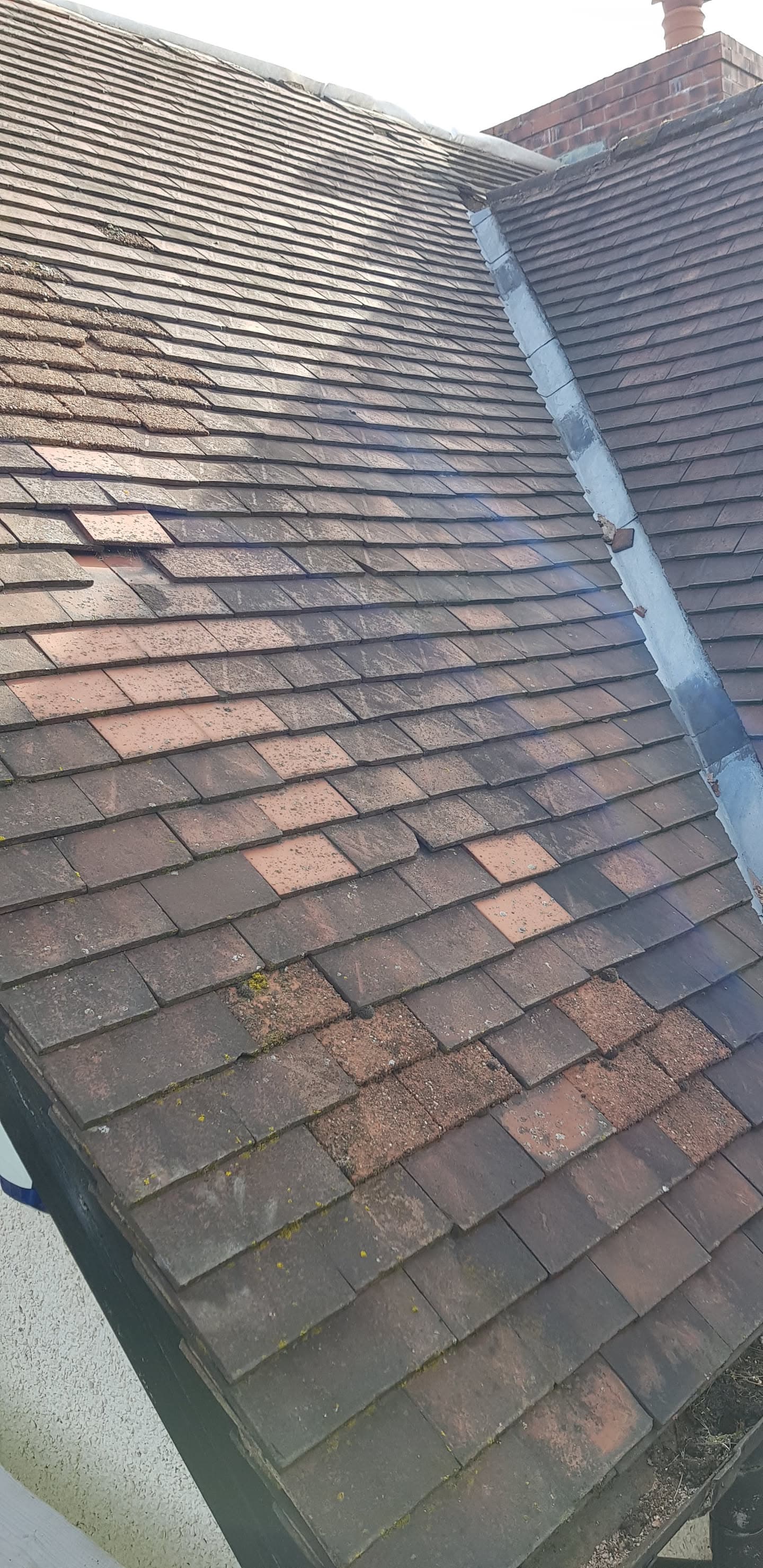 Pitched roof with brown concrete tiles and white painted lead valley between two roof sections