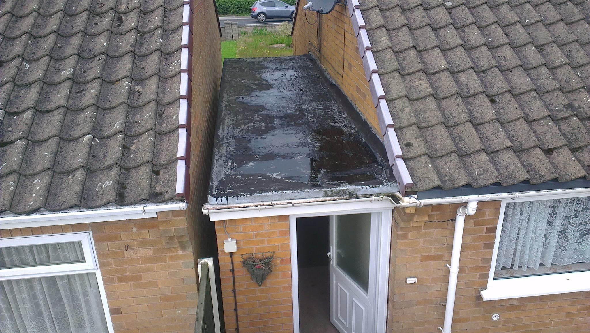 Flat roof porch extension with dark felt covering between two pitched tiled roofs