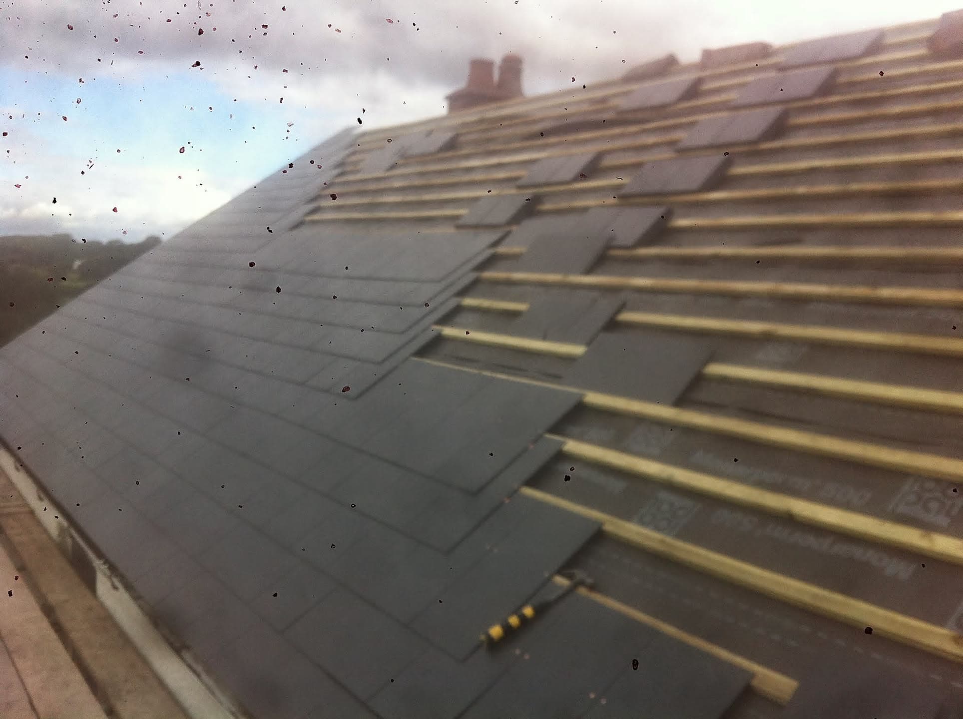 Pitched roof with grey slate tiles being installed on timber battens