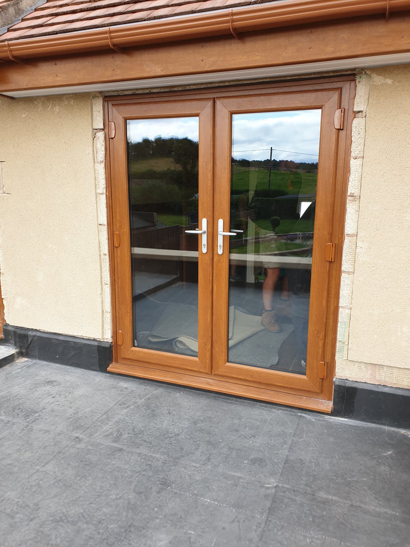 Flat roof with grey felt surface and wooden French doors leading to conservatory