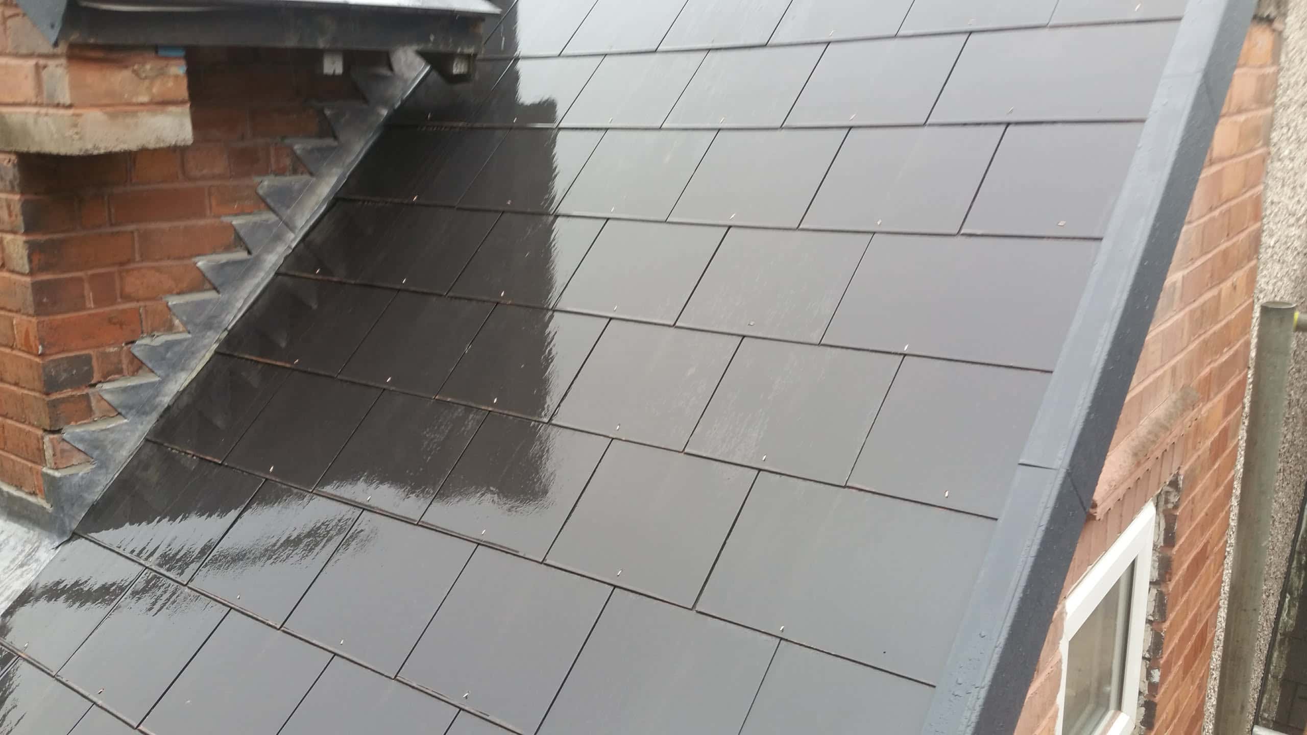 Pitched roof with grey slate tiles and lead flashing around brick chimney